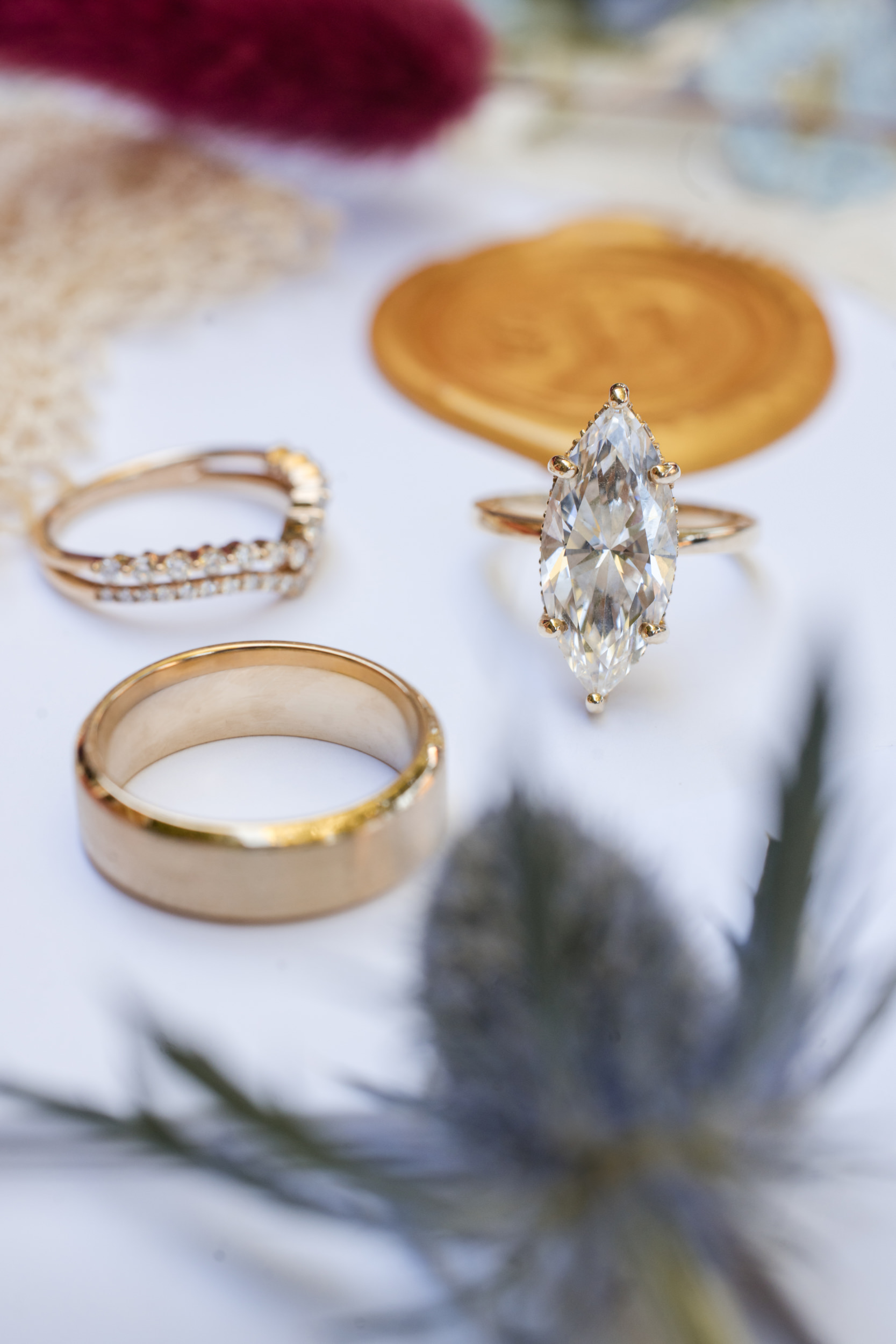 Three rings—a gold band, a diamond-studded ring, and a marquise-cut diamond solitaire—displayed on a white surface with decorative accents, perfect for capturing the elegance of a Leoness Cellars wedding.