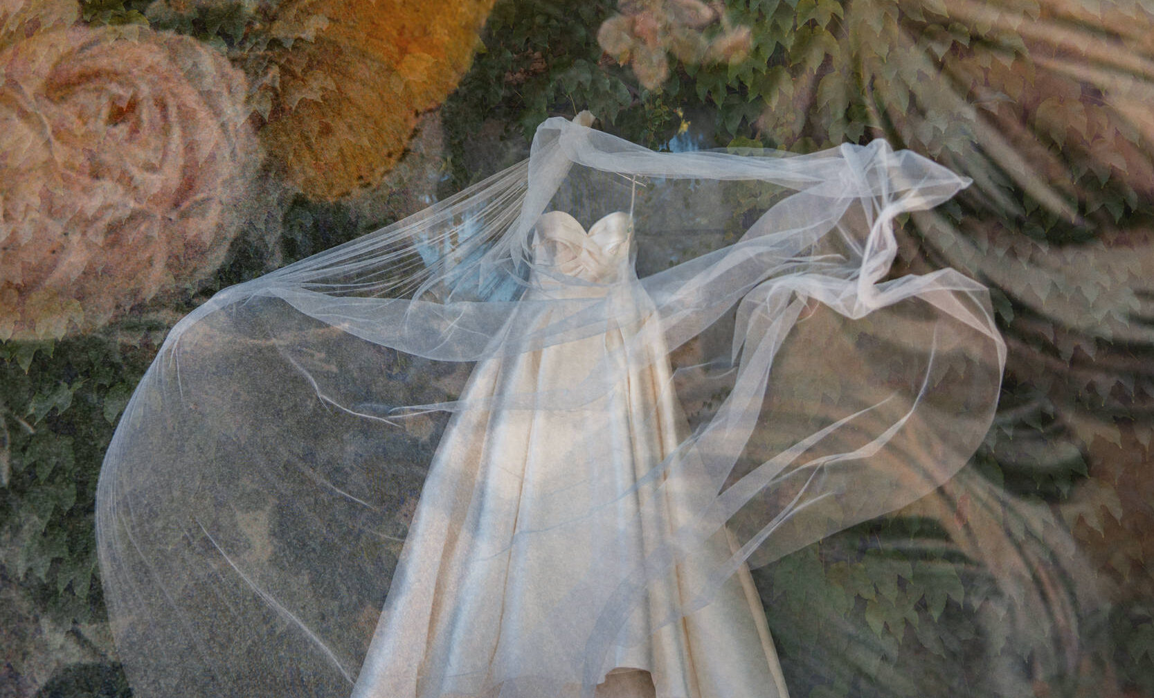 A white strapless dress with a long, flowing veil is displayed against a background of a large, detailed floral tapestry, capturing the elegance of a Leoness Cellars wedding.