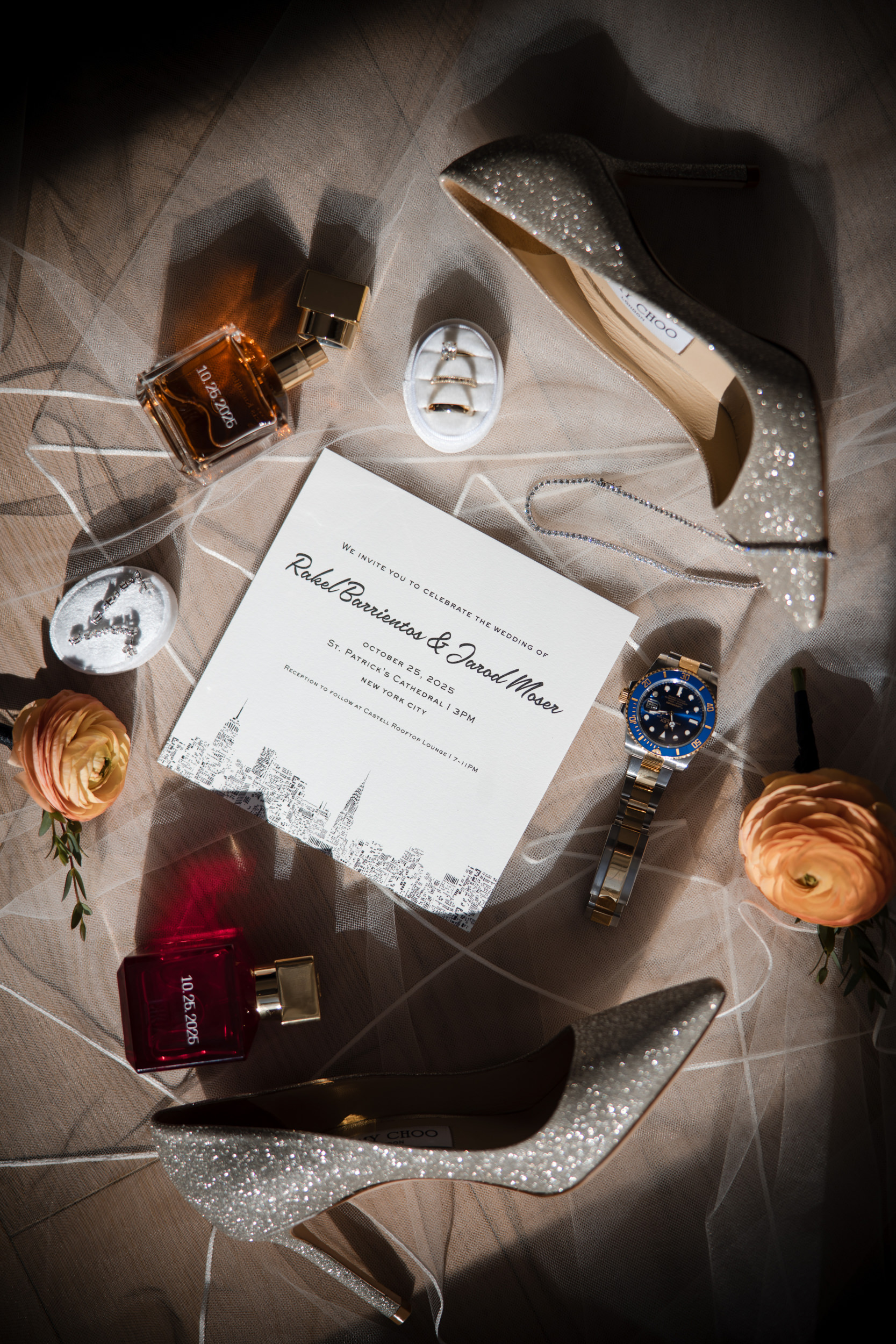 Flat lay of a wedding invitation, sparkling heels, perfume bottles, a wristwatch, flowers, rings in a box, and decorative stones on tulle—perfect inspiration for a Castell Rooftop Lounge or St. Patrick’s Cathedral wedding.