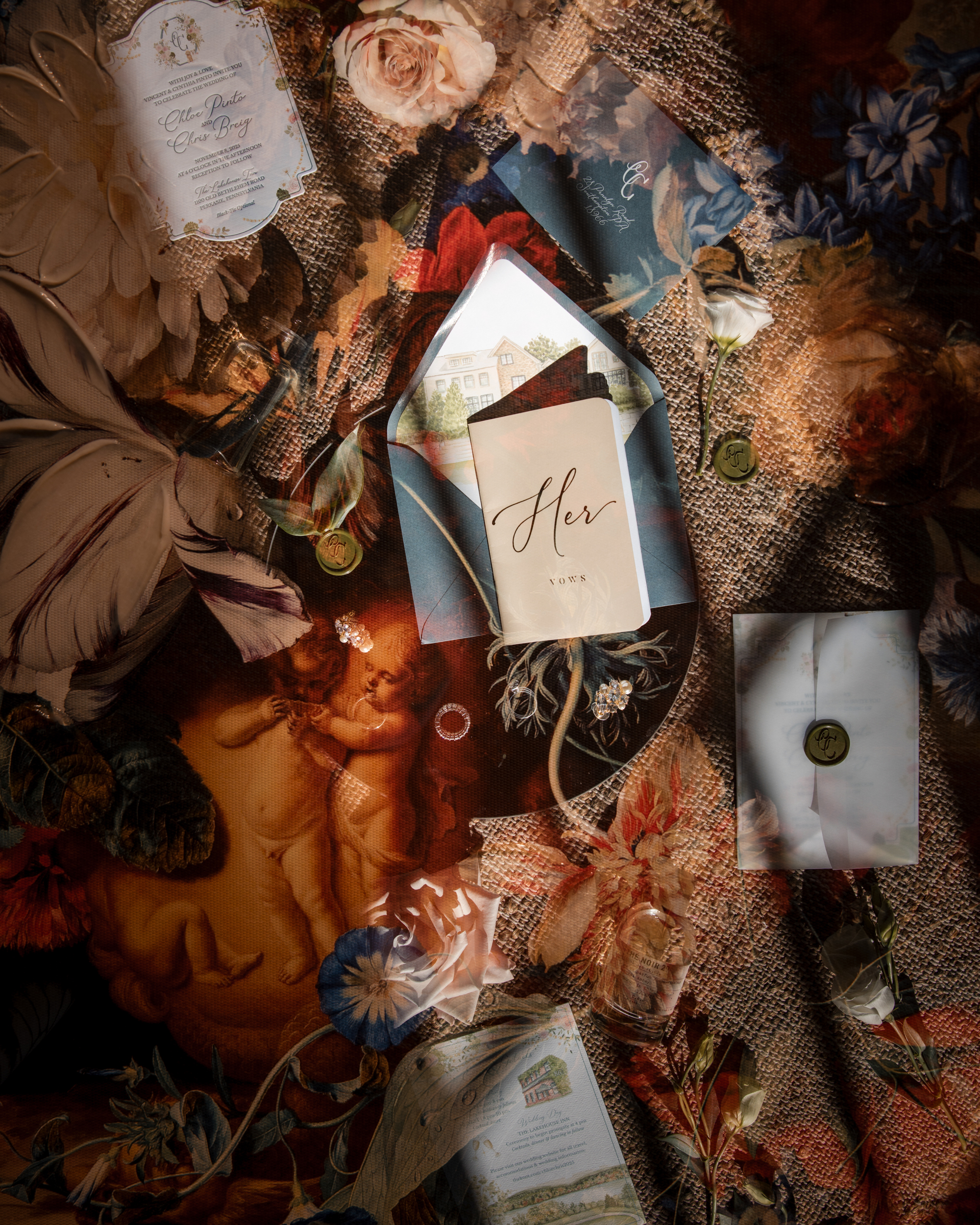A collection of wedding stationery, flowers, and wax-sealed envelopes is arranged on a floral and classical art-themed surface in warm, soft lighting—perfect inspiration for an elegant Lake House Inn wedding.
