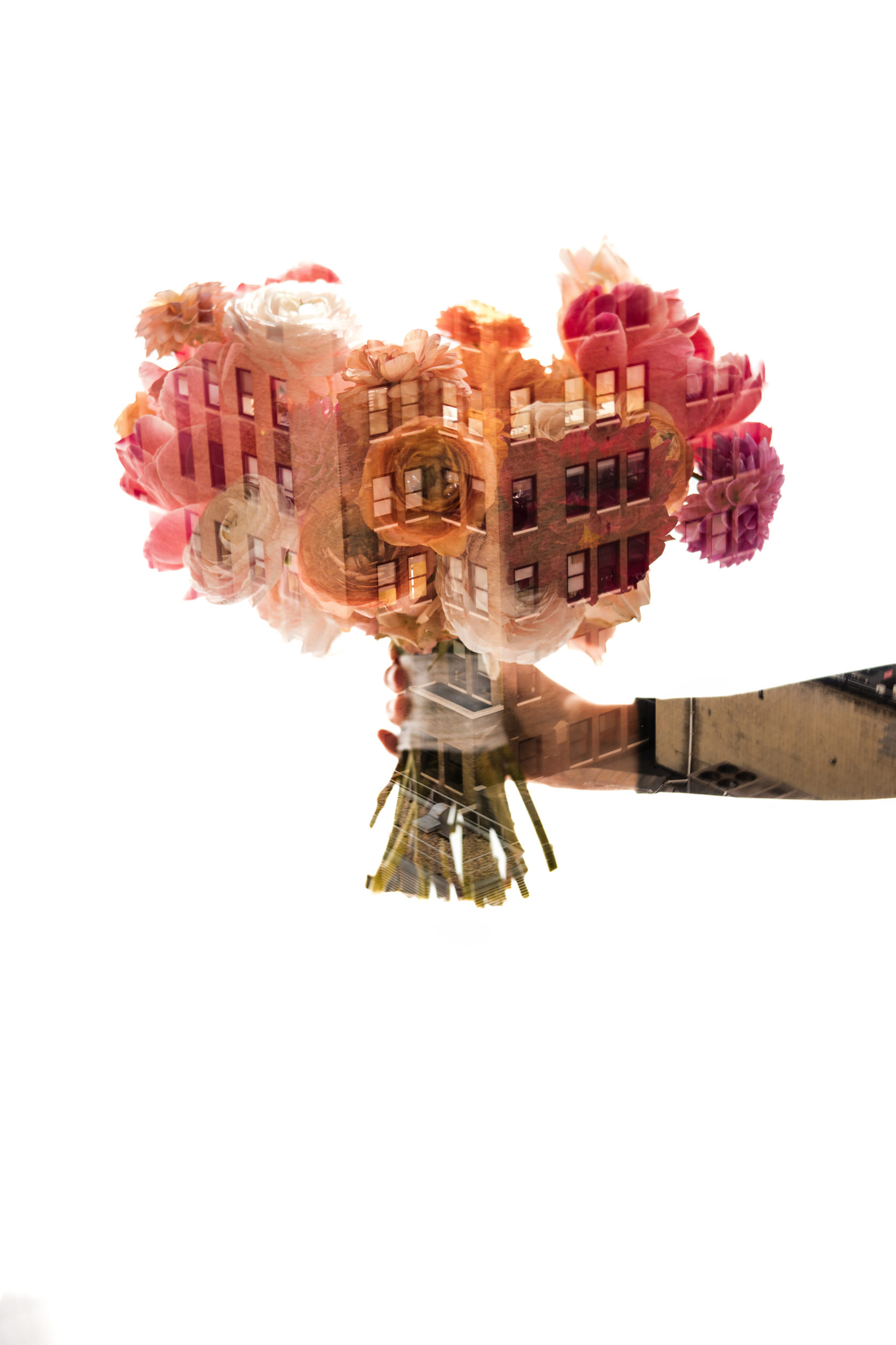 A hand holds a bouquet of flowers with a double exposure effect, blending building facades—like those near Castell Rooftop Lounge—into the blooms against a white background.
