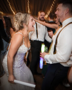 A woman in a white dress laughs energetically while dancing with a man in formal attire at a lively Lake House Inn wedding. Other guests are dancing in the background, adding to the joyful atmosphere.