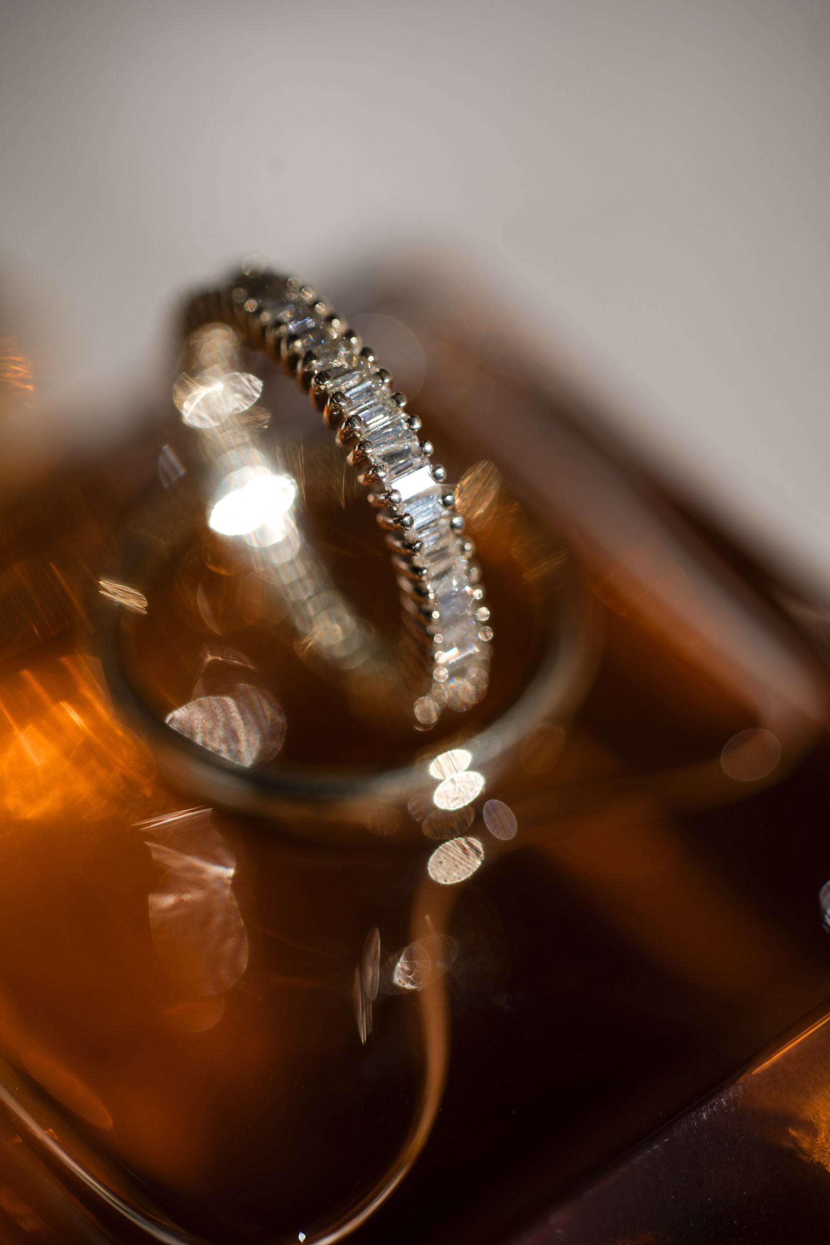 A close-up of a diamond-studded ring resting on a glass bottle, with a warm, blurred background and reflective light spots—perfect for capturing the elegance of a Castell Rooftop Lounge St. Patrick’s Cathedral wedding.