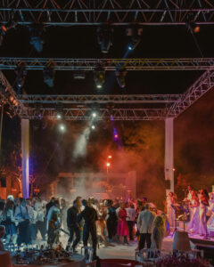 People dancing under stage lights at a nighttime event with a live band performing on stage; smoke effects and lighting create a festive atmosphere reminiscent of a Villa Ephrussi de Rothschild wedding celebration.