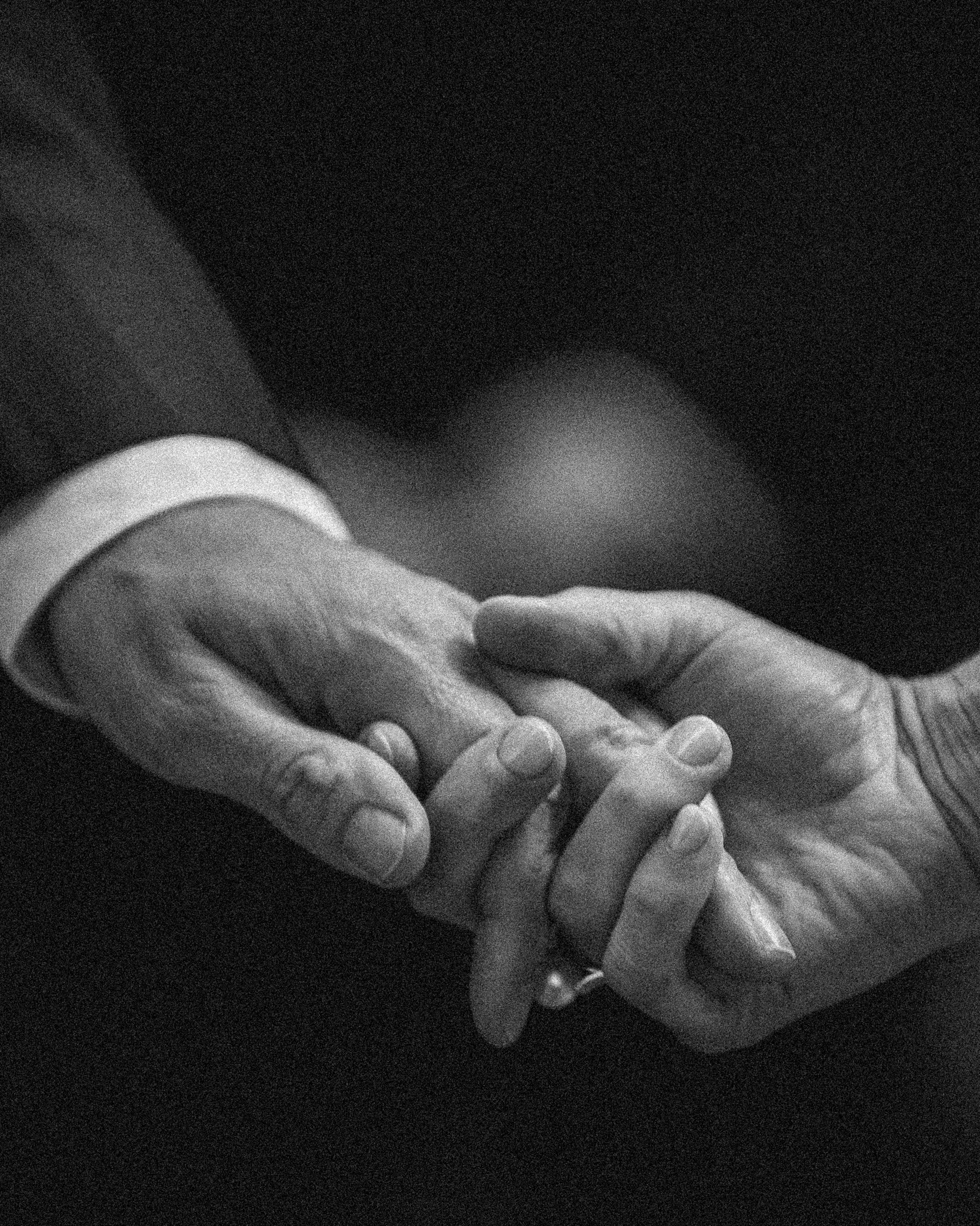 Two people holding hands, one in a suit, create an intimate moment. This black-and-white image captures their connection, making it perfect for a Finland destination wedding against a dramatic dark background.