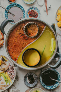 A hot pot divided into two broths, one red and one yellow, with ingredients and dipping sauces in small bowls arranged around it on a table—perfect for sharing at a cozy liberty warehouse wedding.