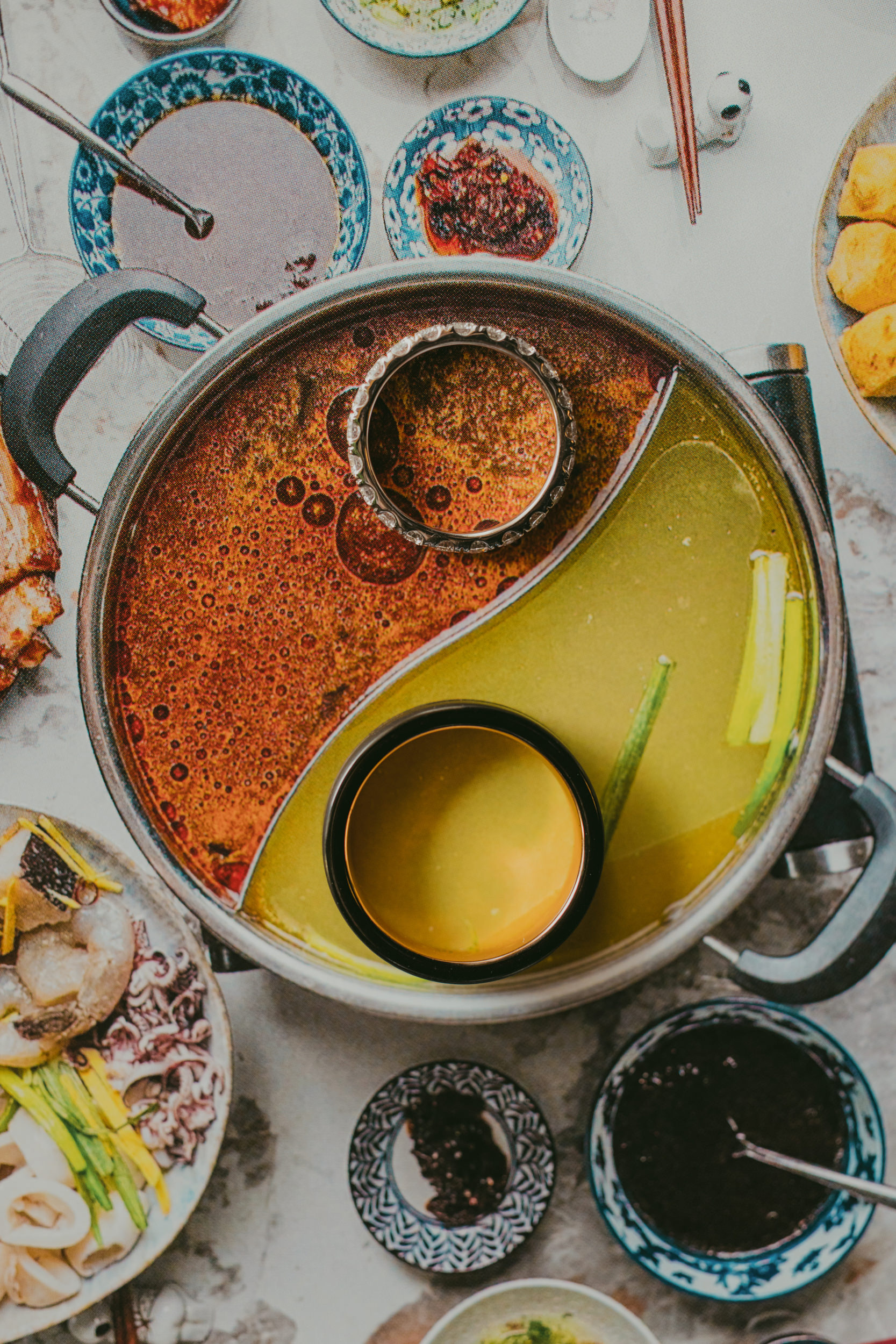 A hot pot divided into two broths, one red and one yellow, with ingredients and dipping sauces in small bowls arranged around it on a table—perfect for sharing at a cozy liberty warehouse wedding.
