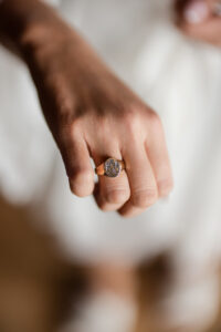 A close-up of a hand wearing a gold ring with an engraved design, captured at a Liberty Warehouse wedding, against a blurred background.