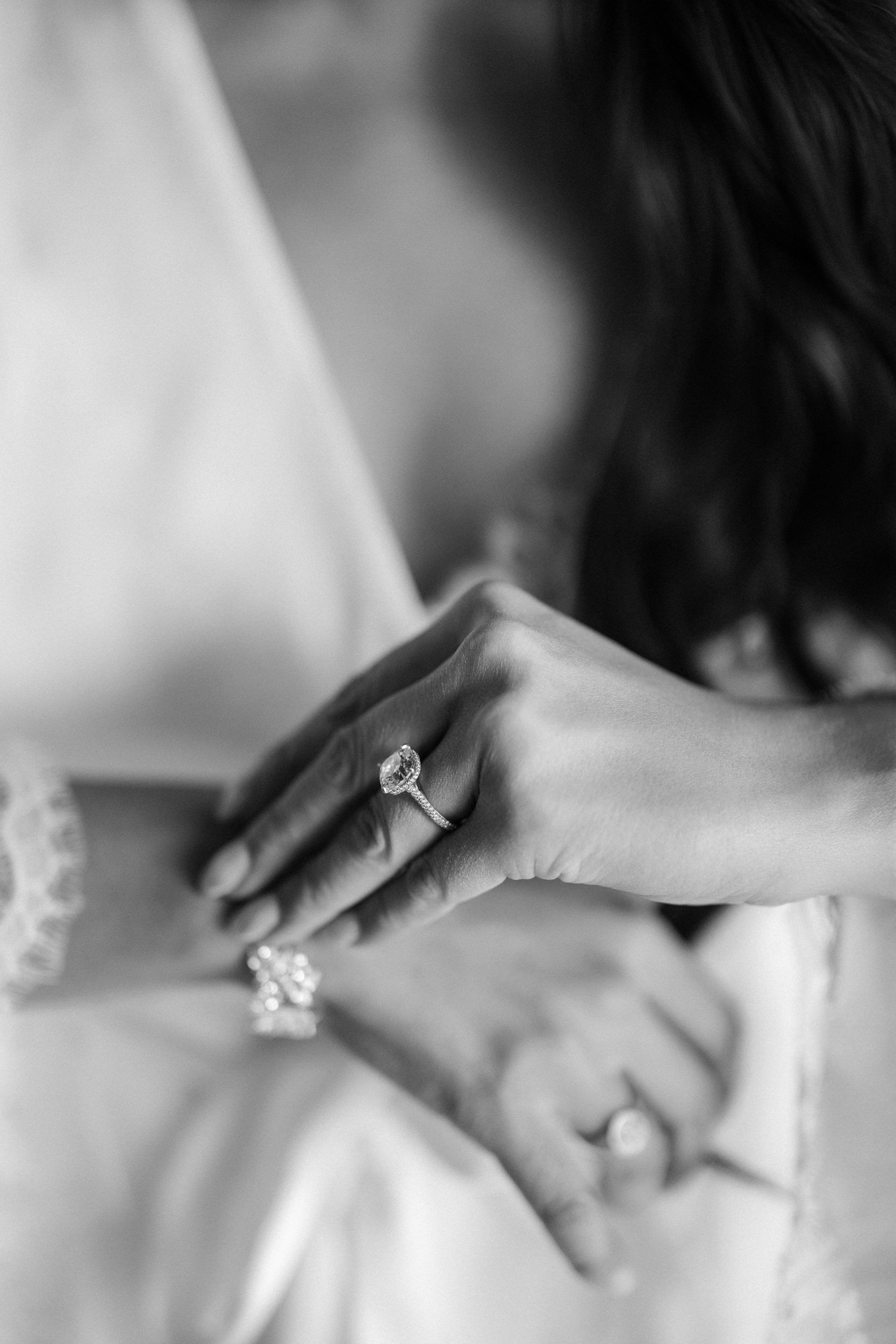 A close-up black and white photo shows two hands, both with rings, gently touching each other—capturing the intimate moments of a Liberty Warehouse wedding.