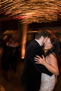 A bride and groom dance closely at their Liberty Warehouse wedding reception, smiling and surrounded by blurred lights and guests in the background.