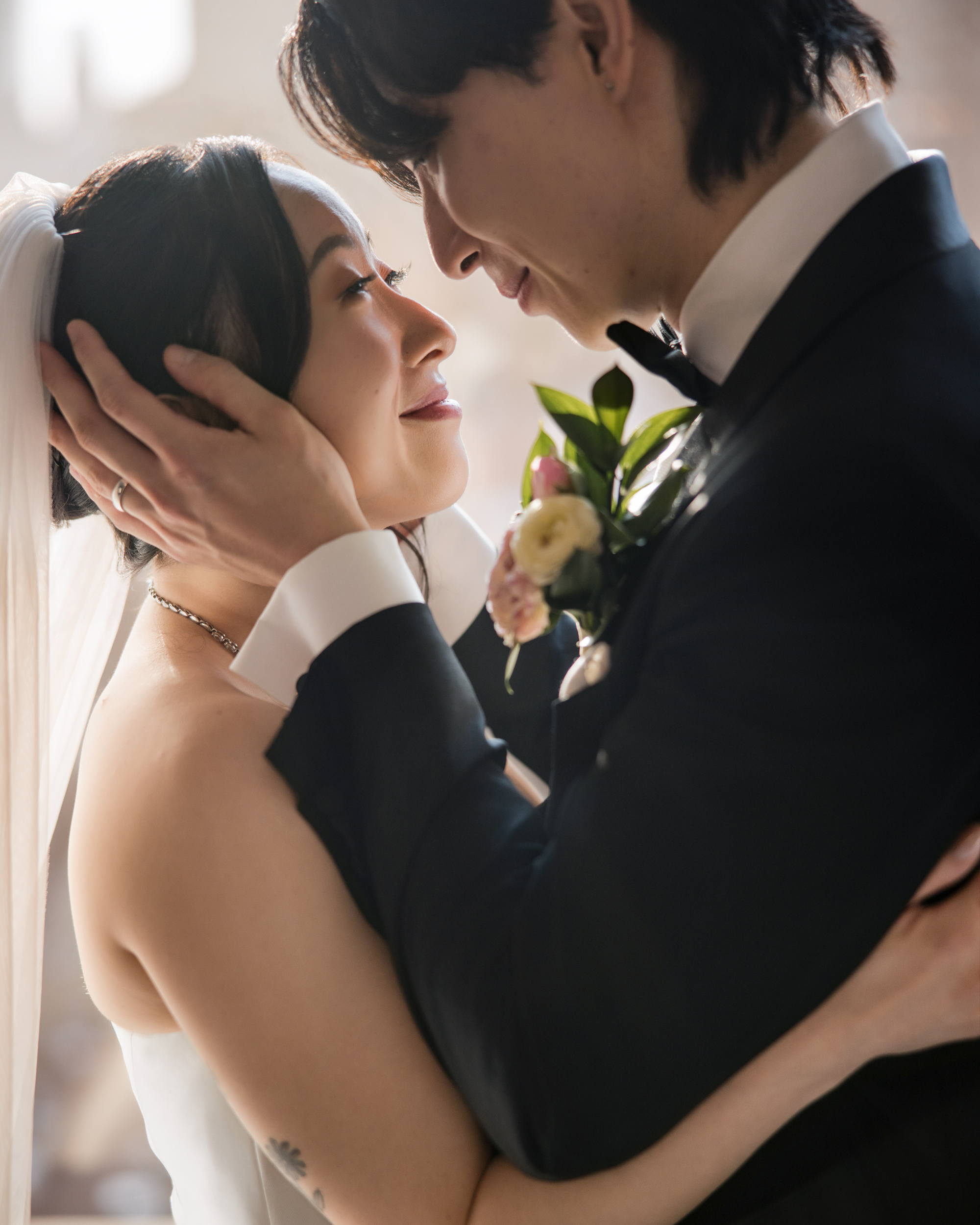 A bride and groom in formal attire embrace closely, looking into each other's eyes with soft natural light in the background at their Downtown Club Philadelphia wedding.