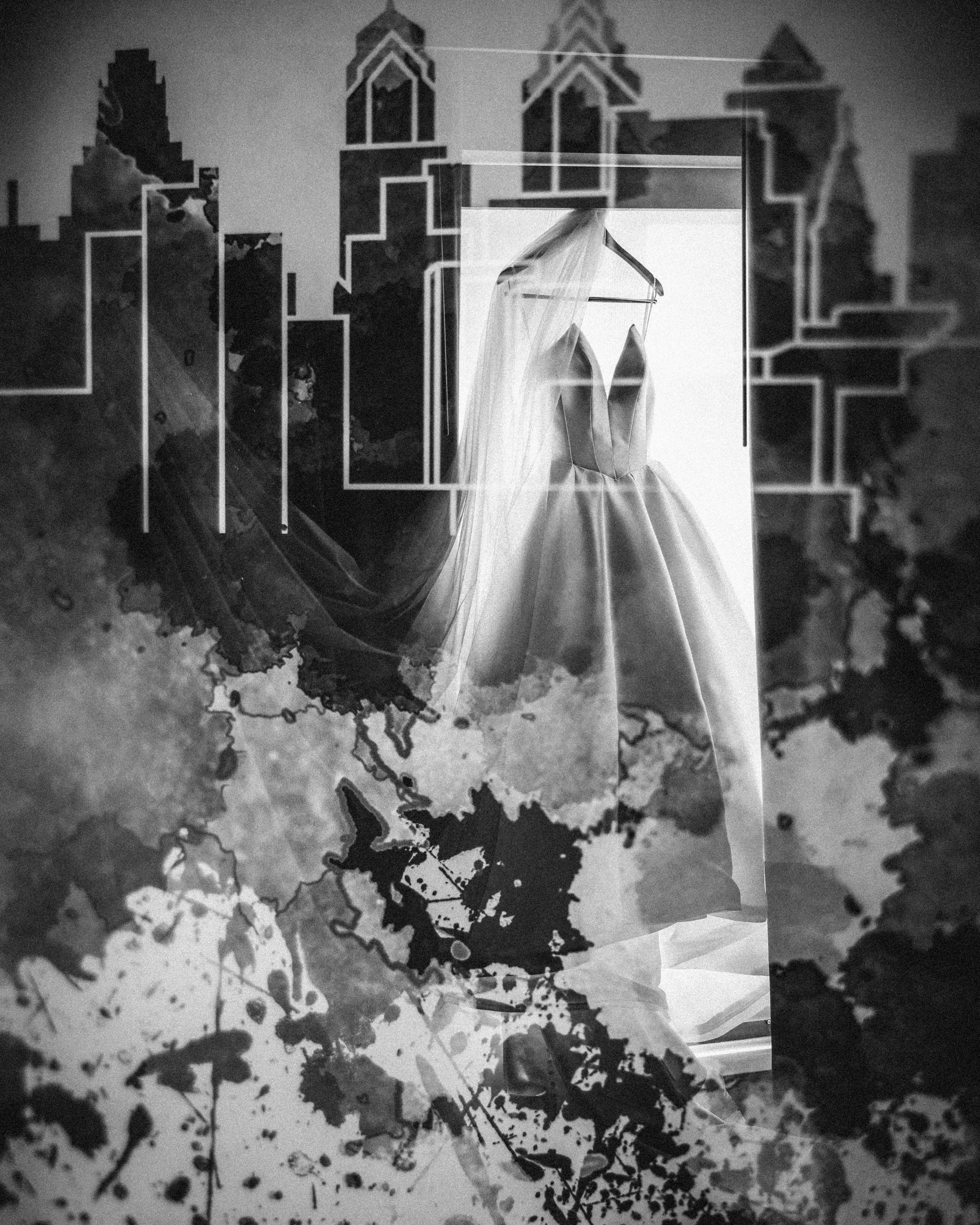 A wedding dress on a hanger, framed by a city skyline outline and abstract black ink splatters in a grayscale composition—a chic nod to a Downtown Club Philadelphia Wedding.
