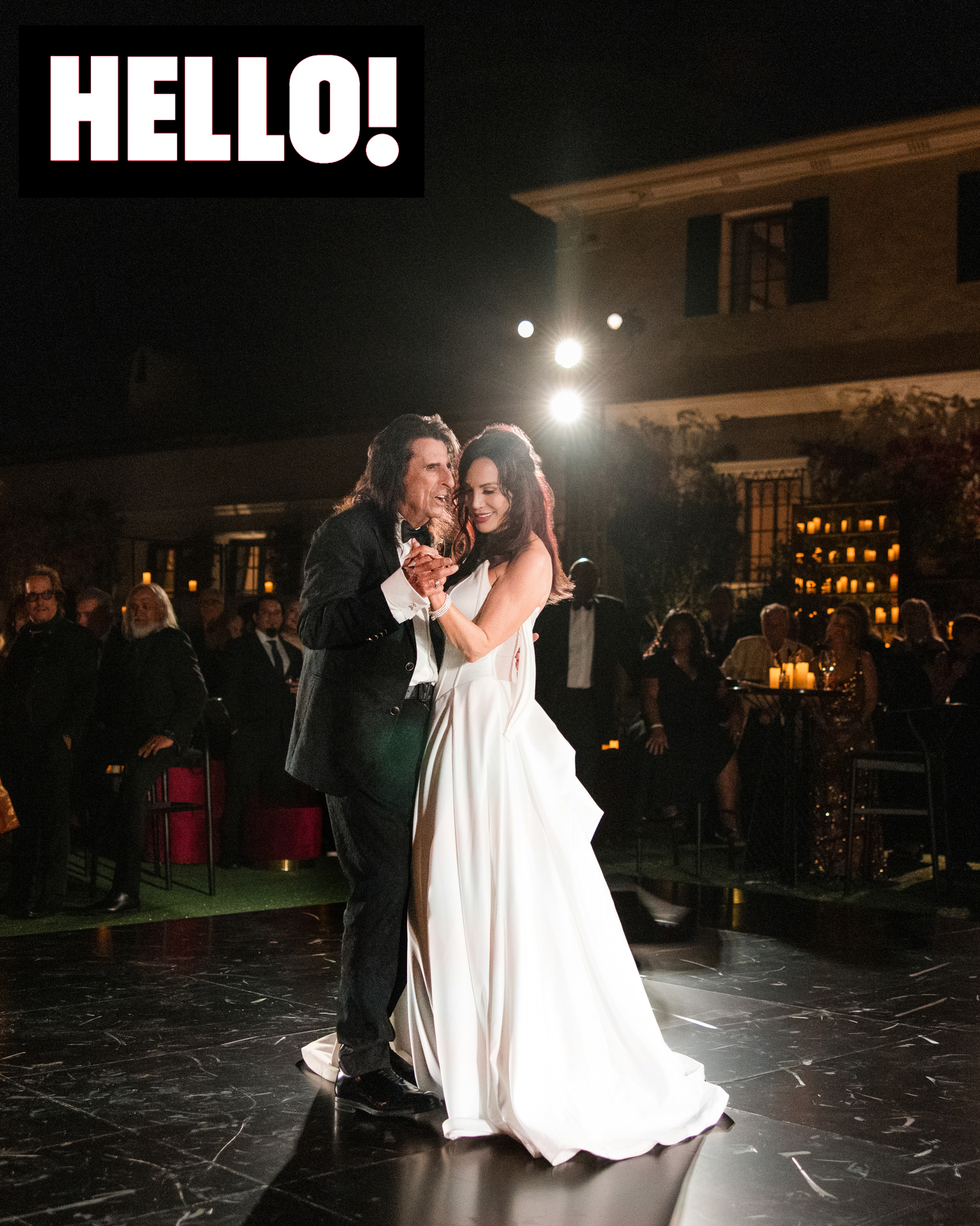 Alice Cooper and Sheryl Cooper share a dance on a black floor at an evening Wrigley Mansion wedding reception with seated guests watching.