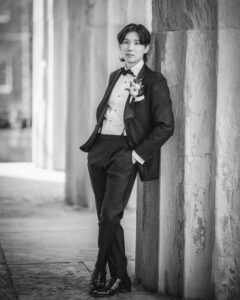 A person in a suit with a bow tie and boutonniere leans against a stone wall in an outdoor setting, posing for Downtown Club Philadelphia wedding second bank photos while looking at the camera.