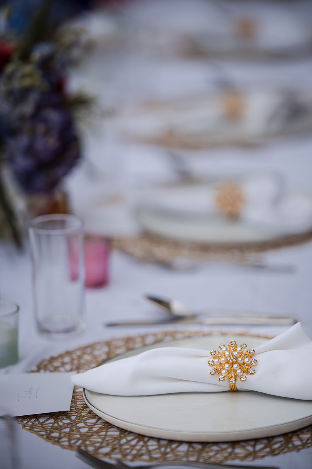 A white napkin with a gold decorative ring is placed on a white plate atop a woven placemat at a formally set dining table, perfect for an elegant St. Thomas wedding.