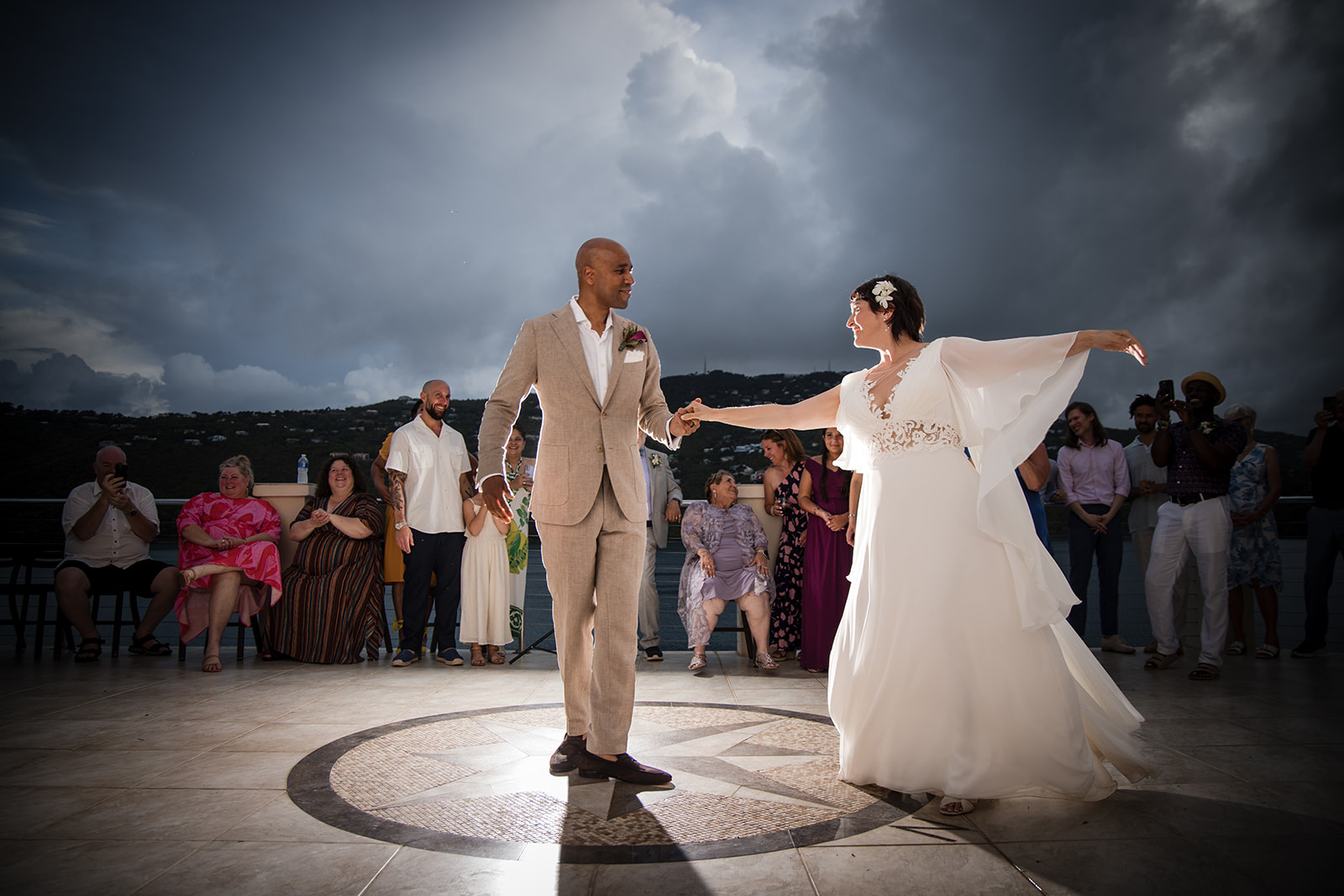 A bride and groom dance together on an outdoor terrace at their St. Thomas wedding, surrounded by guests and set against a backdrop of cloudy skies.