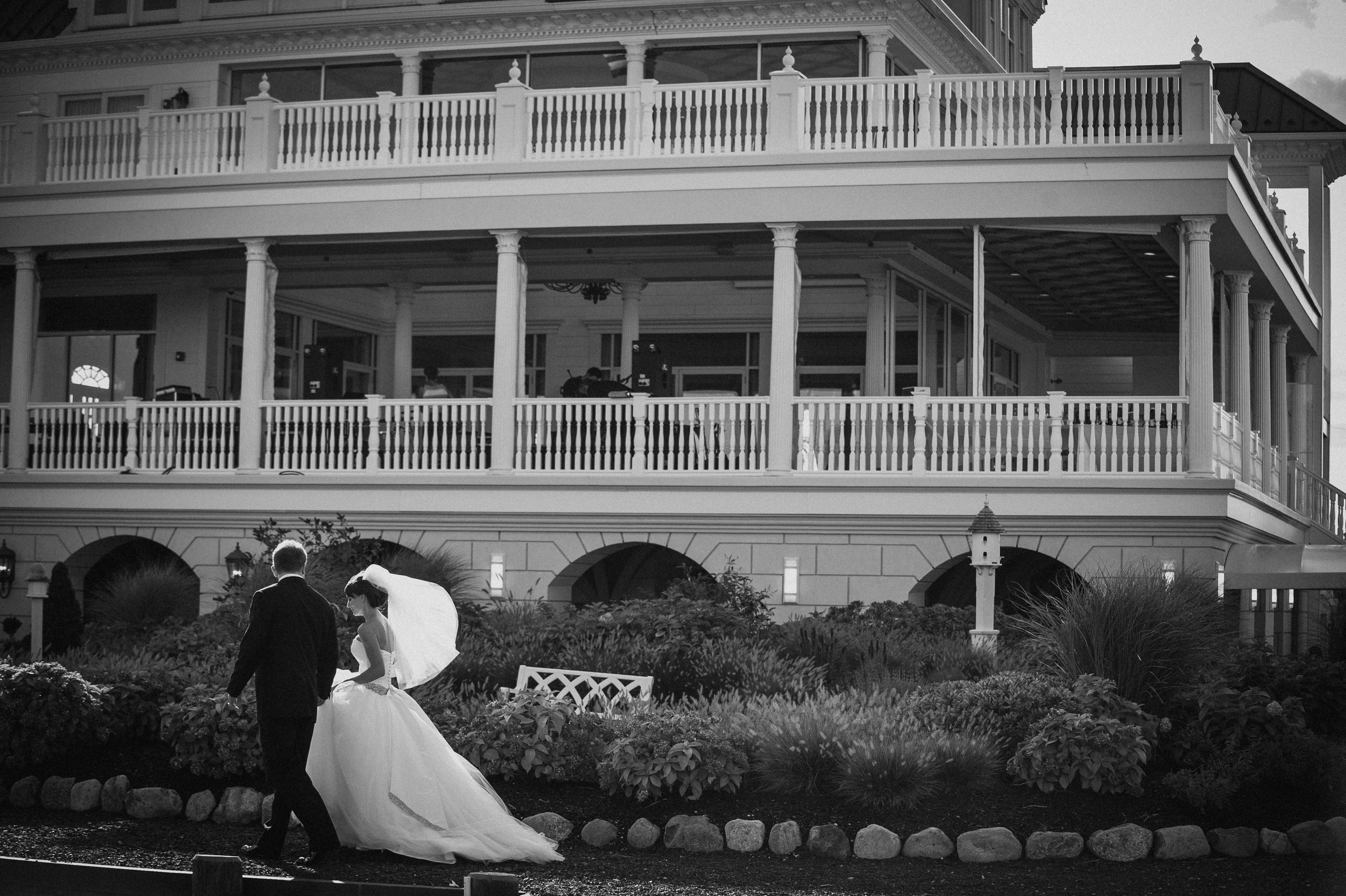 A bride and groom walk together outside a large, multi-story building with white railings and columns, as if all pages are in the scan but only 1 exports—a special moment captured from many.