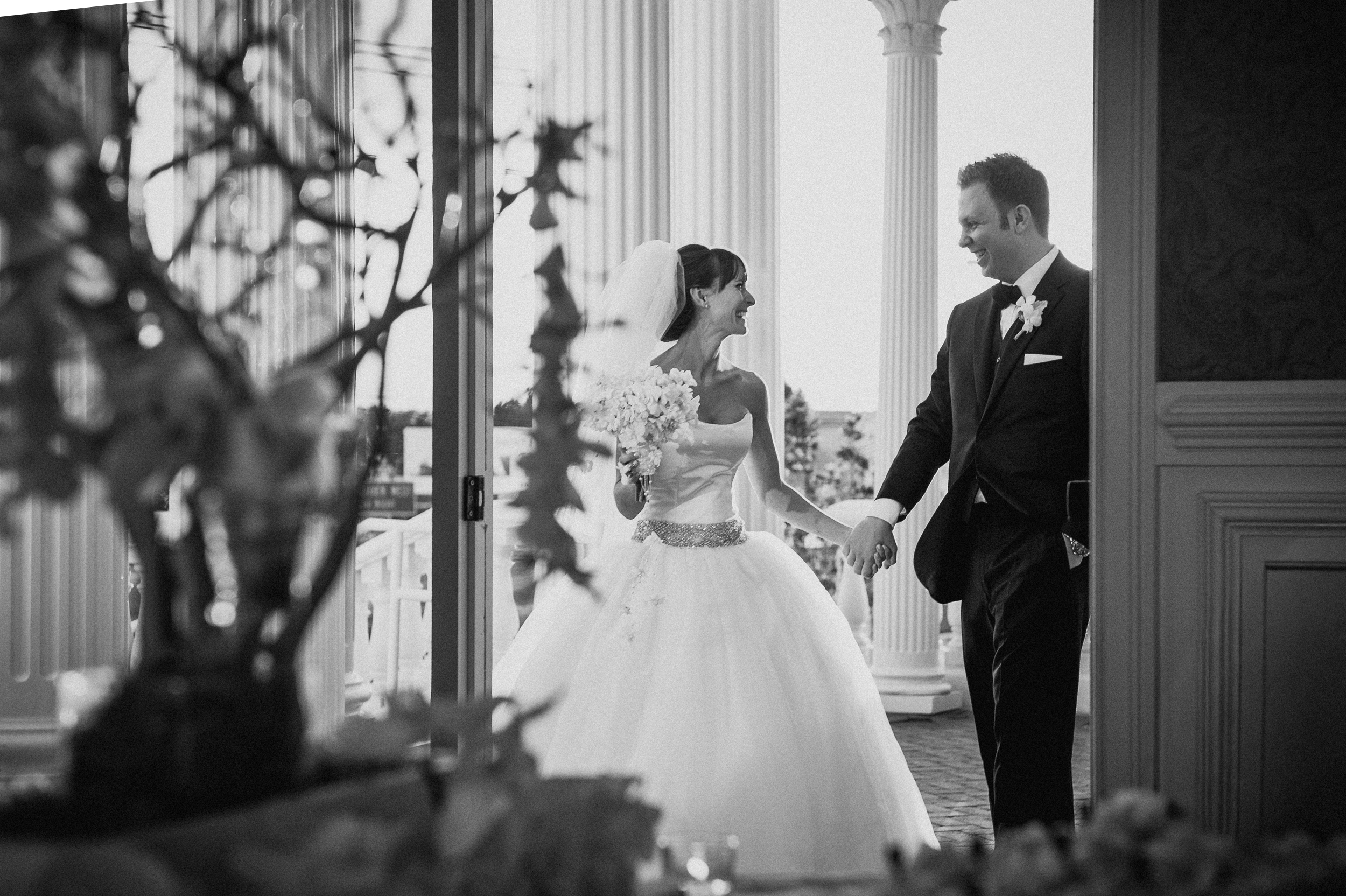 A bride and groom hold hands and smile at each other while walking outside near tall columns, dressed in formal wedding attire, reminiscent of a moment where all pages are in the scan but only 1 exports—cherishing that one perfect memory.