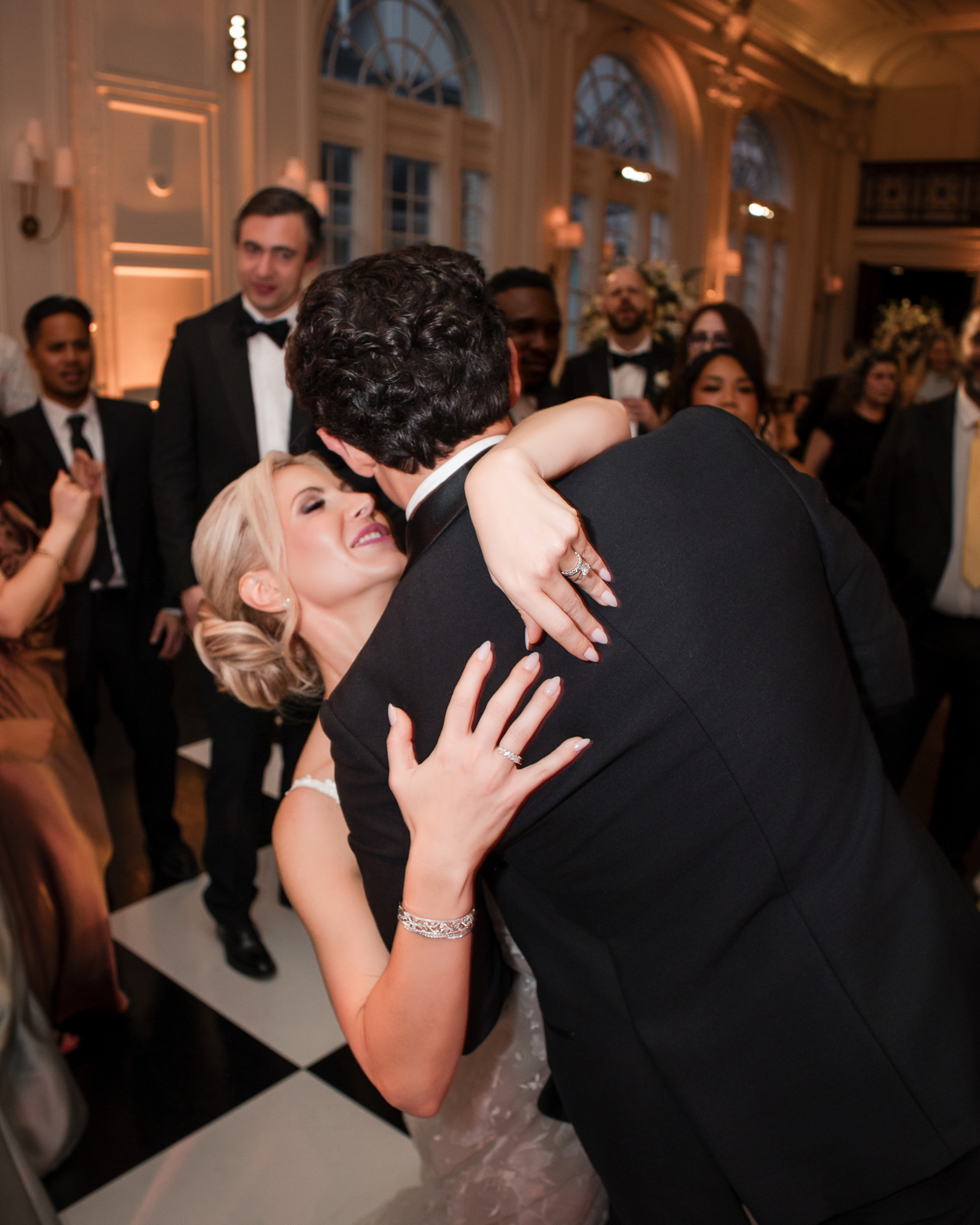 A couple shares a dance at a wedding at XIX in Philadelphia, surrounded by guests in evening attire on a black and white checkered floor.