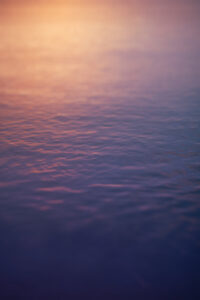 Calm water surface reflecting soft, warm light from the sunset—perfect for a St. Thomas wedding—with gentle ripples and a gradient of purple, blue, and orange hues.