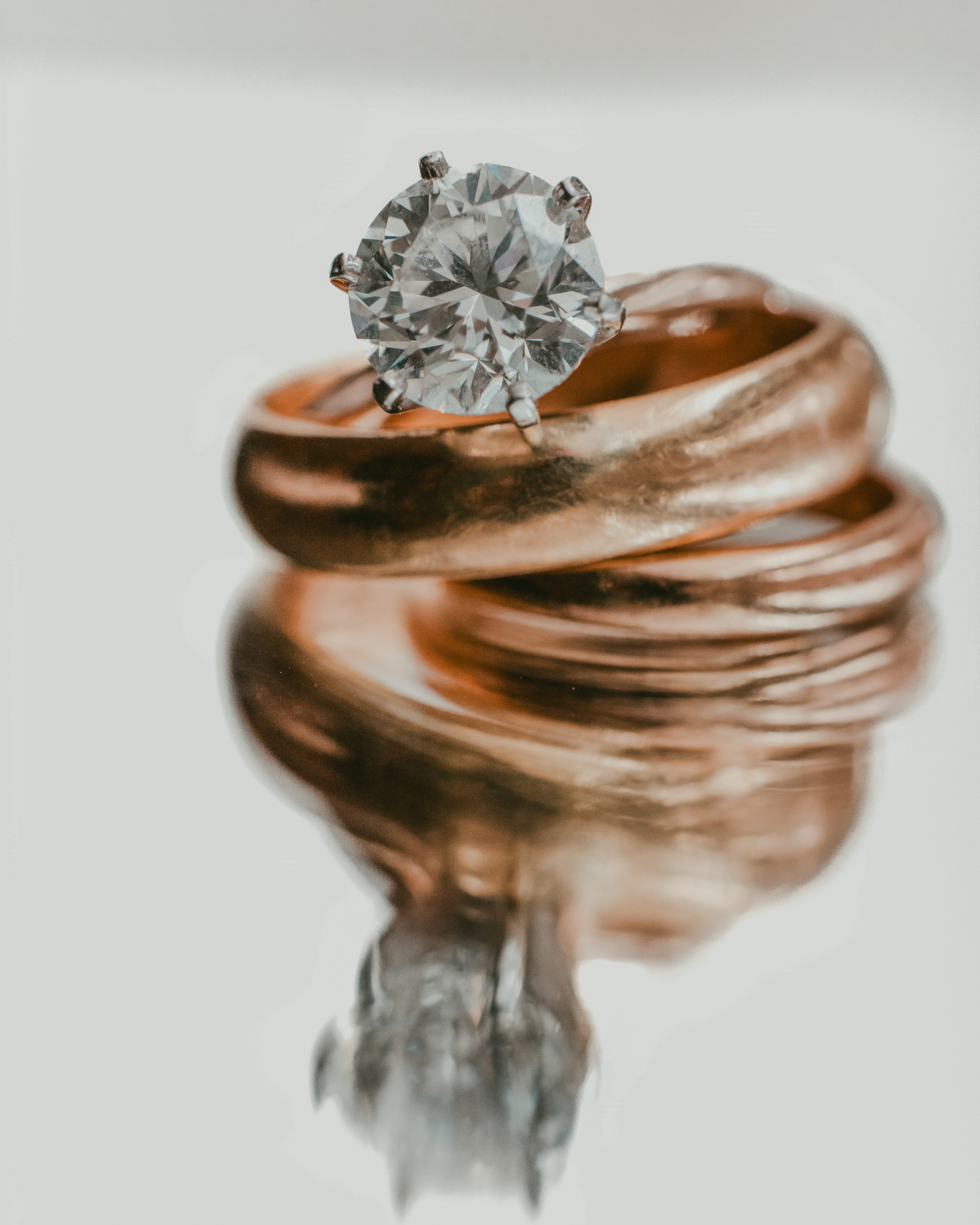 A close-up of a diamond engagement ring stacked on two gold wedding bands at a Pier Sixty and Current Wedding, with their reflection visible on a shiny surface.