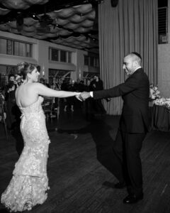 A bride and groom hold hands and dance together on a wooden floor at their Pier Sixty and Current Wedding reception, surrounded by guests.