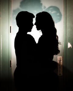 Silhouette of a couple facing each other closely in front of a door with light shining behind them, capturing a romantic moment during an NYC photo walk.