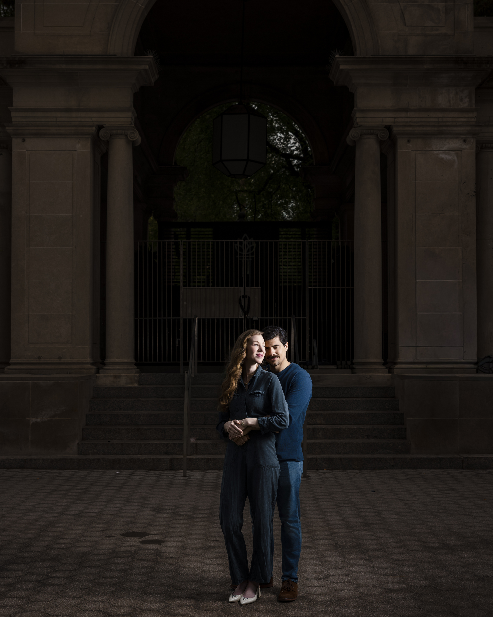 A woman and man stand close together in front of a stone building with large columns and steps, both facing the camera during their NYC photo walk.