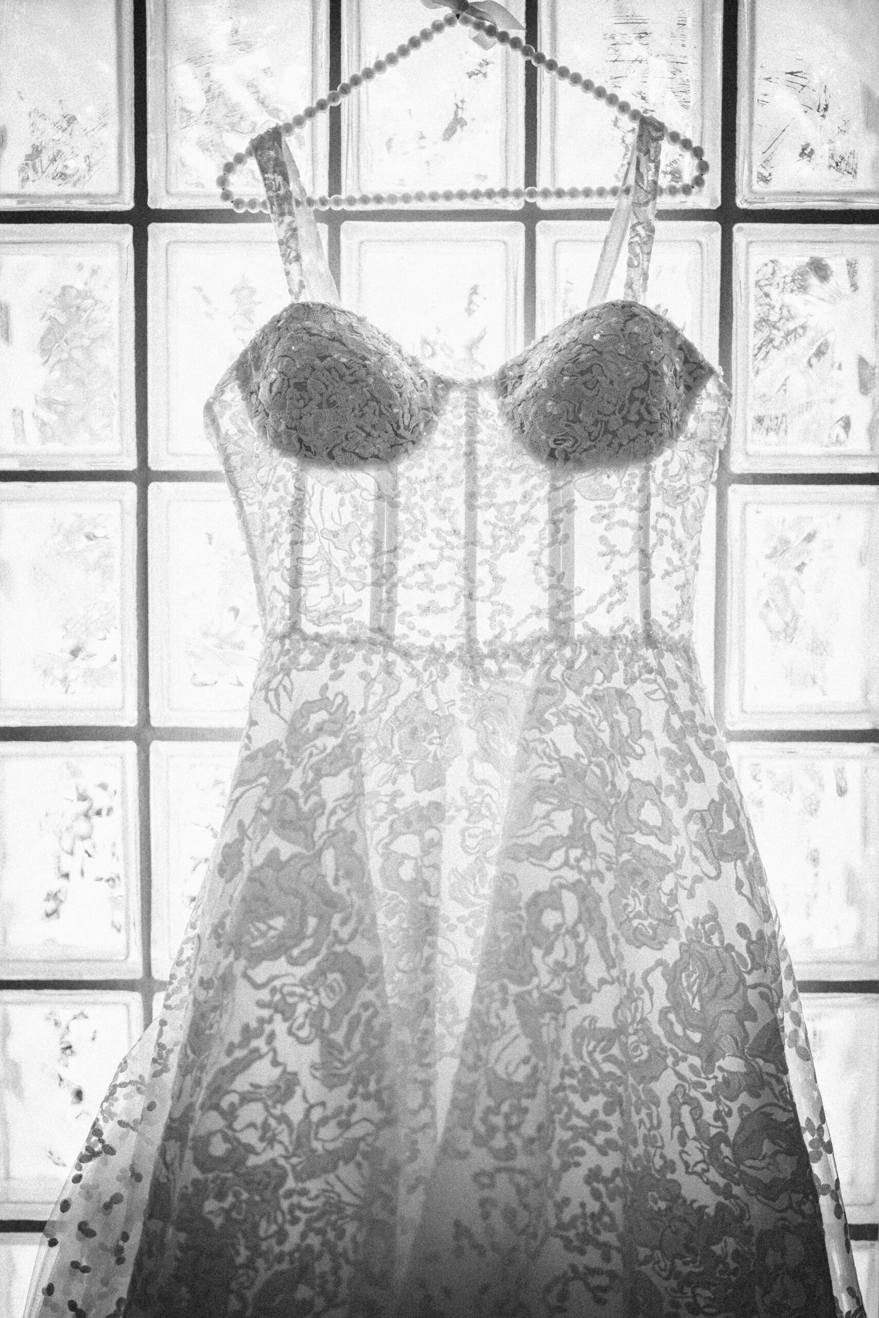 A lace wedding dress on a hanger is displayed in front of frosted glass blocks, with light shining through the fabric, creating a romantic scene reminiscent of a Regatta Place wedding.
