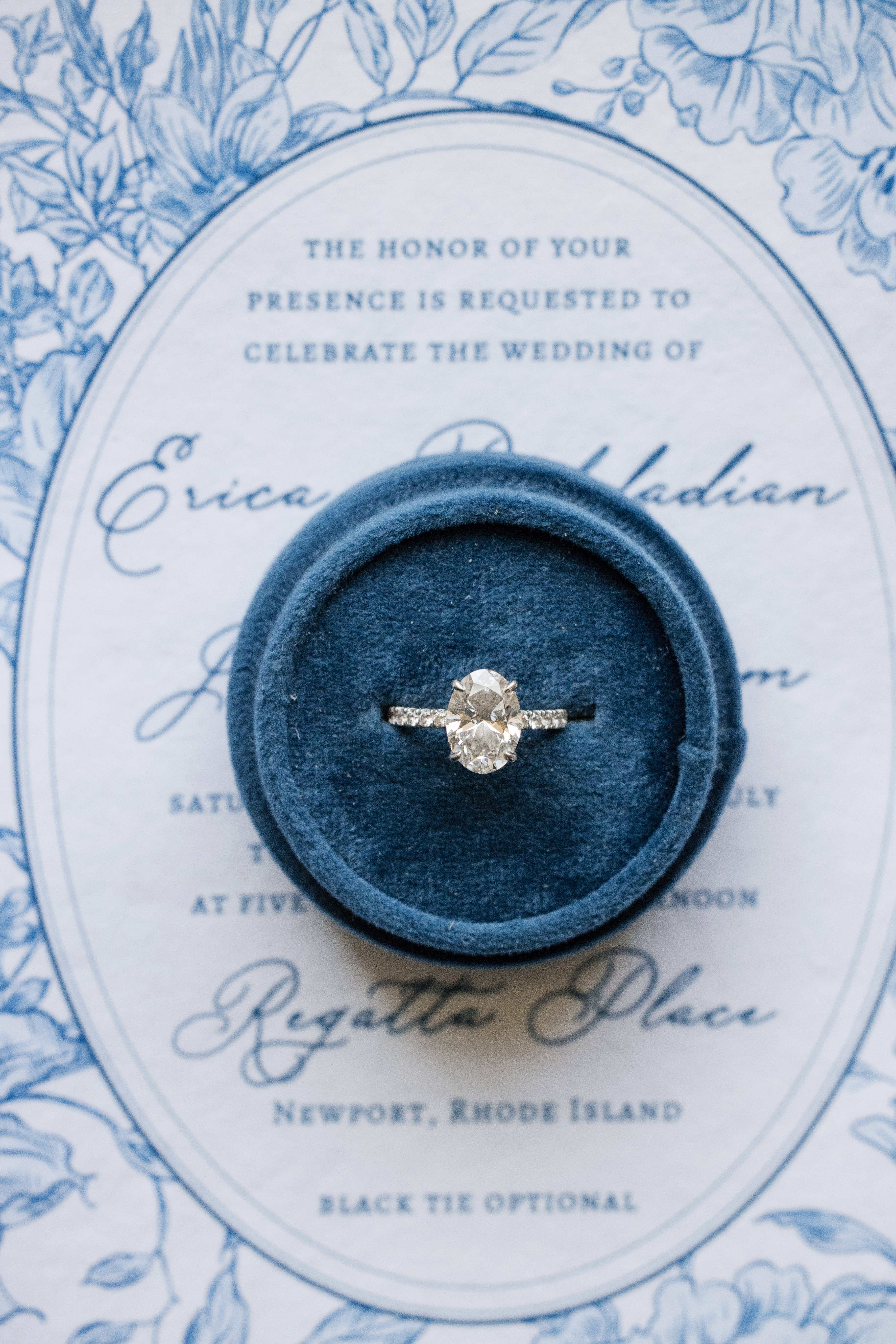 Diamond engagement ring in a blue velvet box placed on a floral wedding invitation, perfect for capturing the elegance of a Regatta Place wedding.