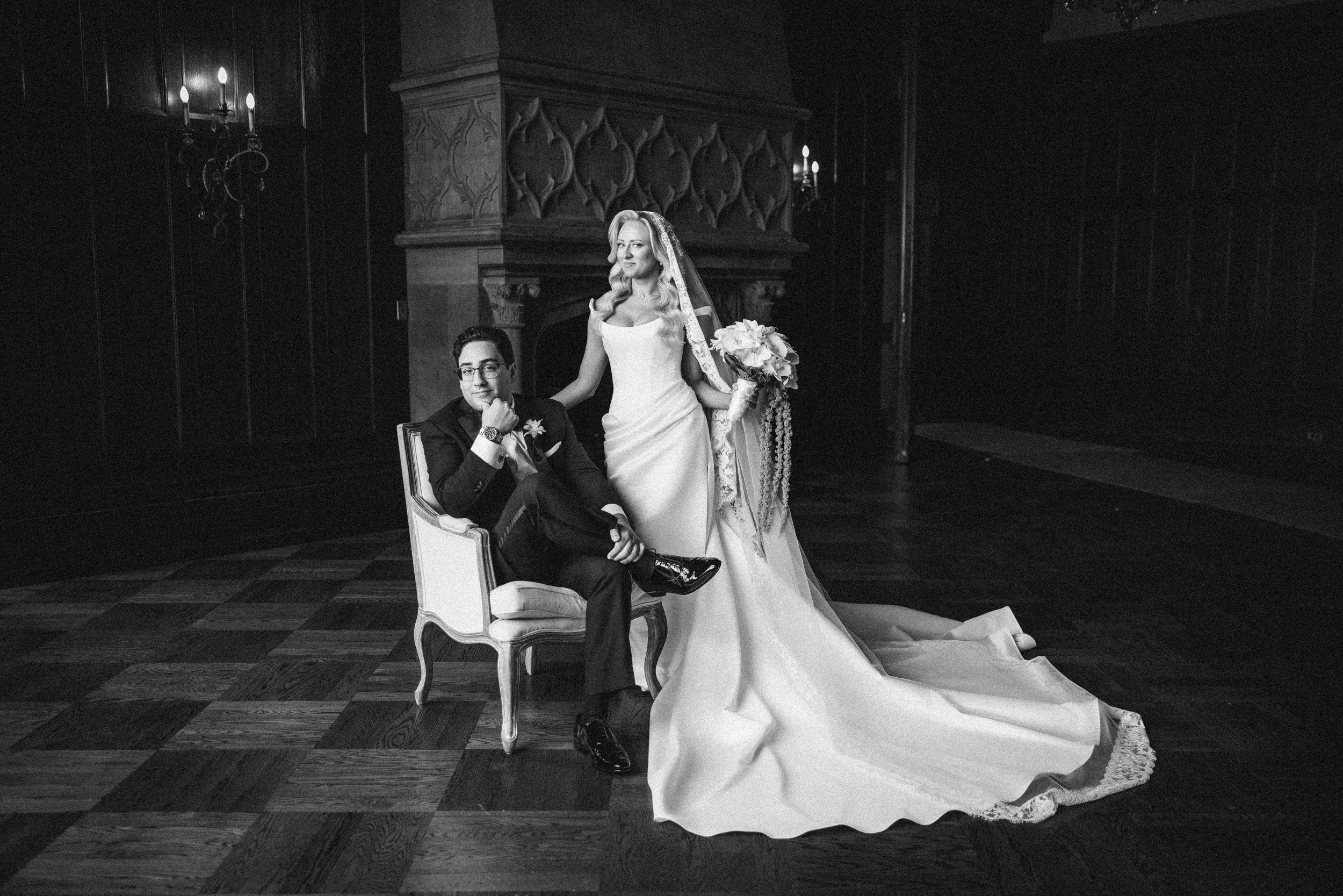 A bride in a long gown stands beside a seated groom in formalwear on a checkered floor in an elegant, dimly lit room, capturing the timeless romance of a Hempstead House at Sands Point Preserve wedding. A bride in a long gown stands beside a seated groom in formalwear on a checkered floor in an elegant, dimly lit room, capturing the timeless romance of a Hempstead House at Sands Point Preserve wedding.