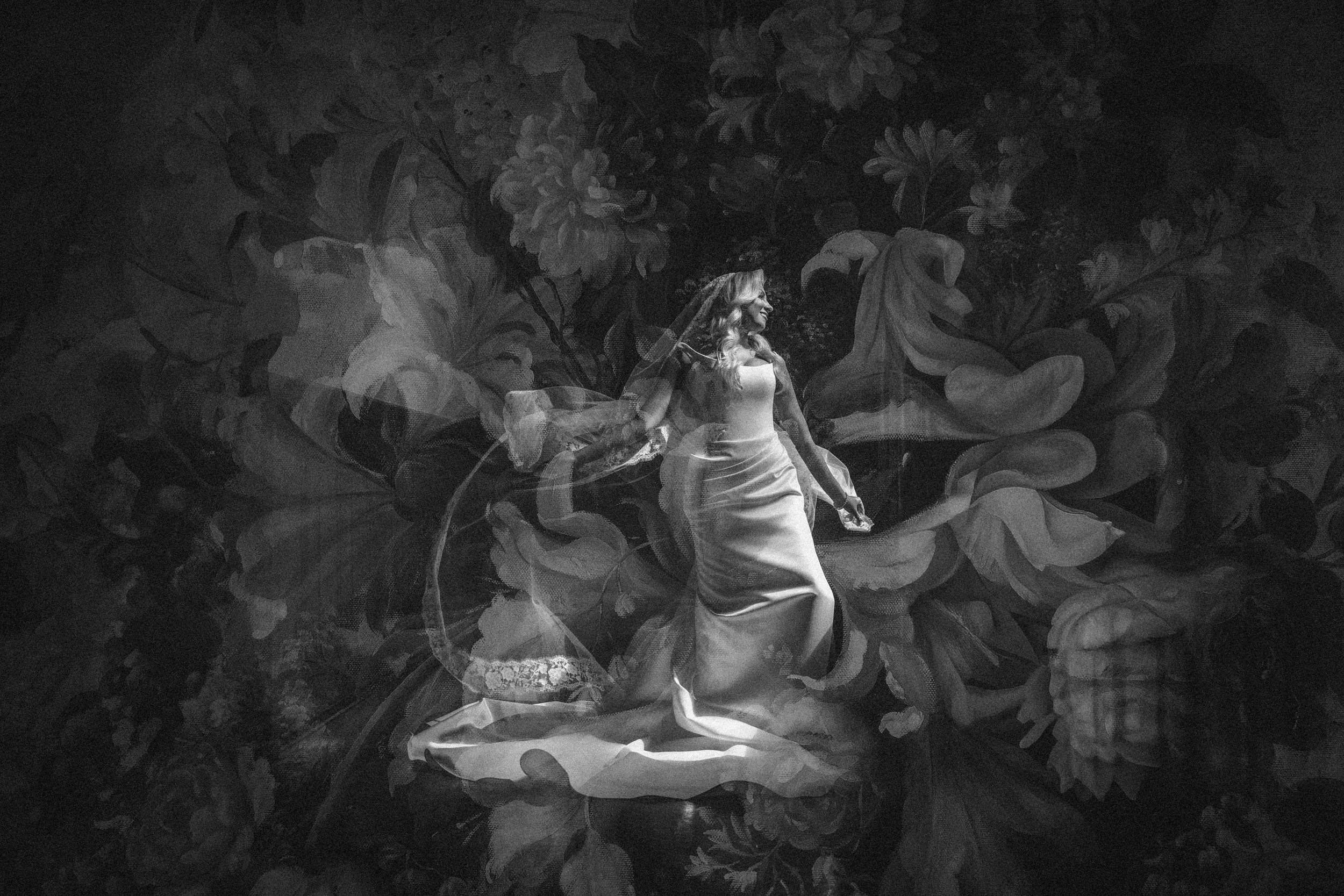 A woman in a gown stands against a floral-patterned background in a black-and-white, double-exposure photograph, evoking the timeless elegance of a Hempstead House at Sands Point Preserve wedding. A woman in a gown stands against a floral-patterned background in a black-and-white, double-exposure photograph, evoking the timeless elegance of a Hempstead House at Sands Point Preserve wedding.