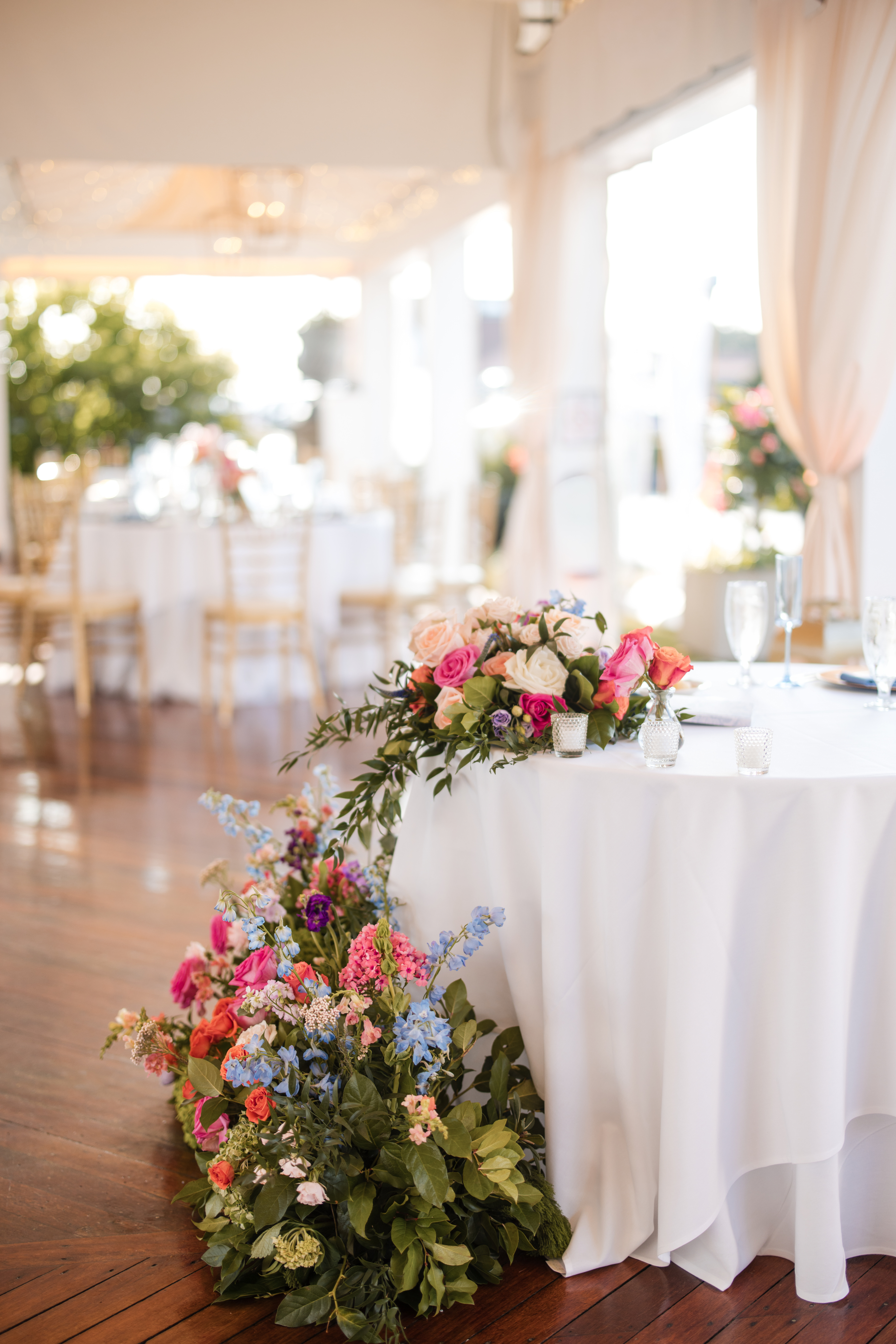 A round table covered with a white tablecloth is decorated with colorful floral arrangements in a bright, elegant banquet hall, creating a charming atmosphere perfect for a Regatta Place wedding.