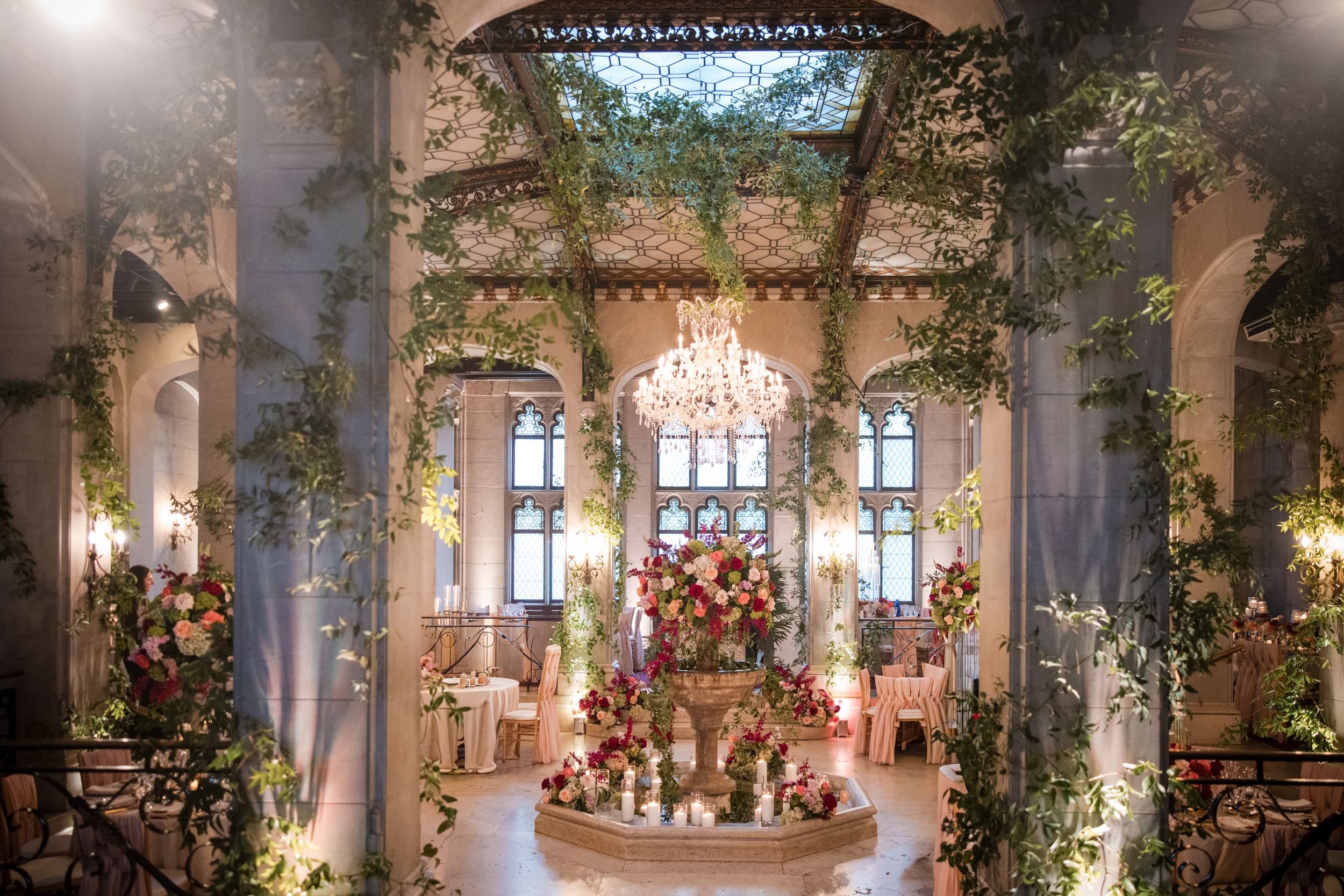 An elegant indoor venue at Hempstead House at Sands Point Preserve, featuring a central floral fountain, chandeliers, arched windows, lush greenery, round tables, and exquisite floral arrangements—perfectly set up for a formal event or an unforgettable wedding. An elegant indoor venue at Hempstead House at Sands Point Preserve, featuring a central floral fountain, chandeliers, arched windows, lush greenery, round tables, and exquisite floral arrangements—perfectly set up for a formal event or an unforgettable wedding.