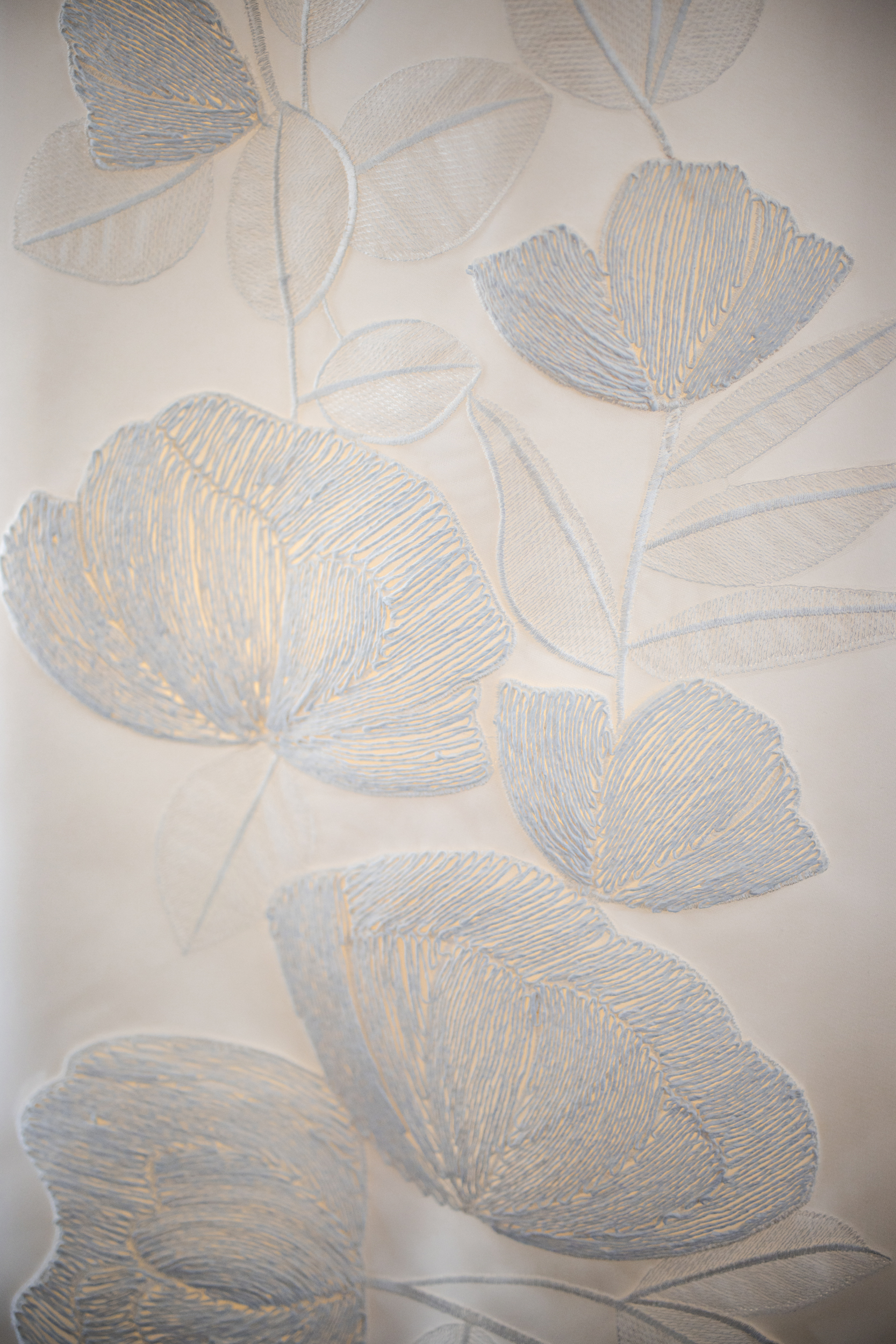 Close-up of a white fabric with delicate, light blue floral embroidery, reminiscent of an elegant Lotte New York Palace wedding, showing large and small flowers with detailed stitching and graceful leaf patterns.