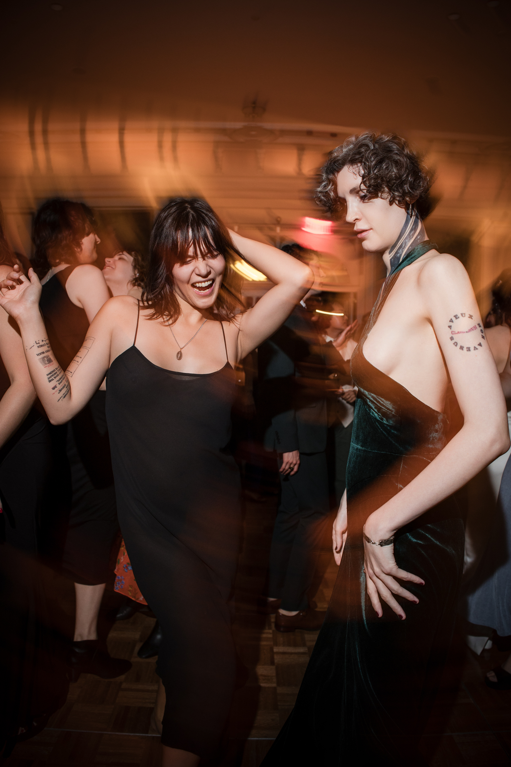 Two people in evening dresses dance energetically at an indoor event, with blurred lights and other guests in the background, capturing the lively atmosphere of a Lotte New York Palace wedding.