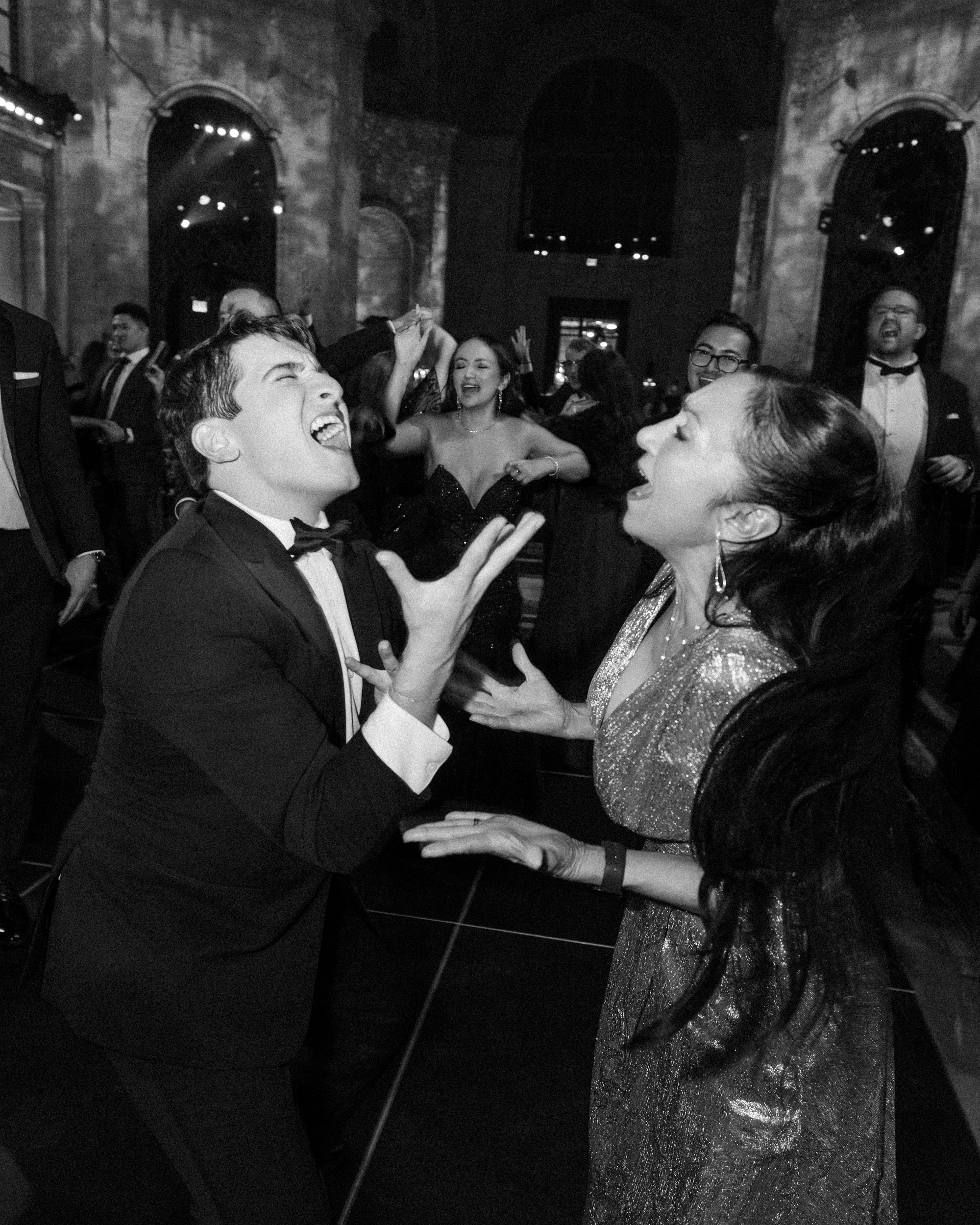 A man in a tuxedo and a woman in a shimmering gown laughing and dancing at a Cipriani 25 Broadway wedding.
