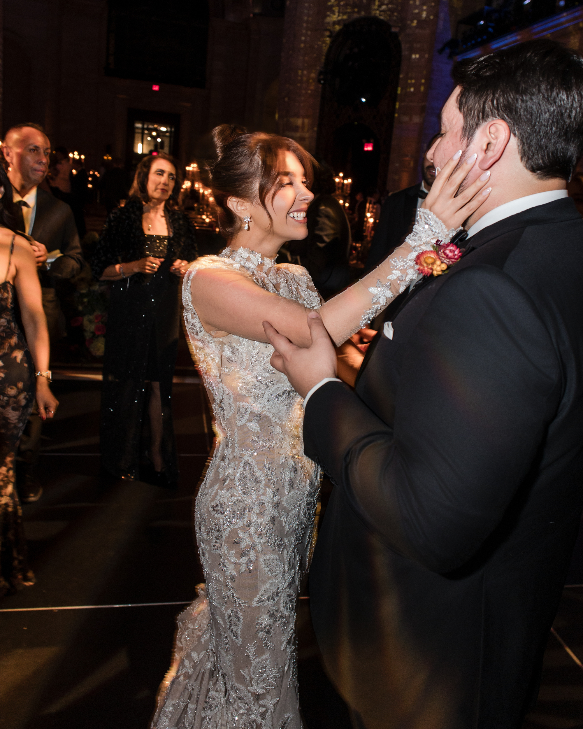 A bride in a lace gown smiles while touching the face of her groom in a tuxedo during a Cipriani 25 Broadway wedding evening reception.