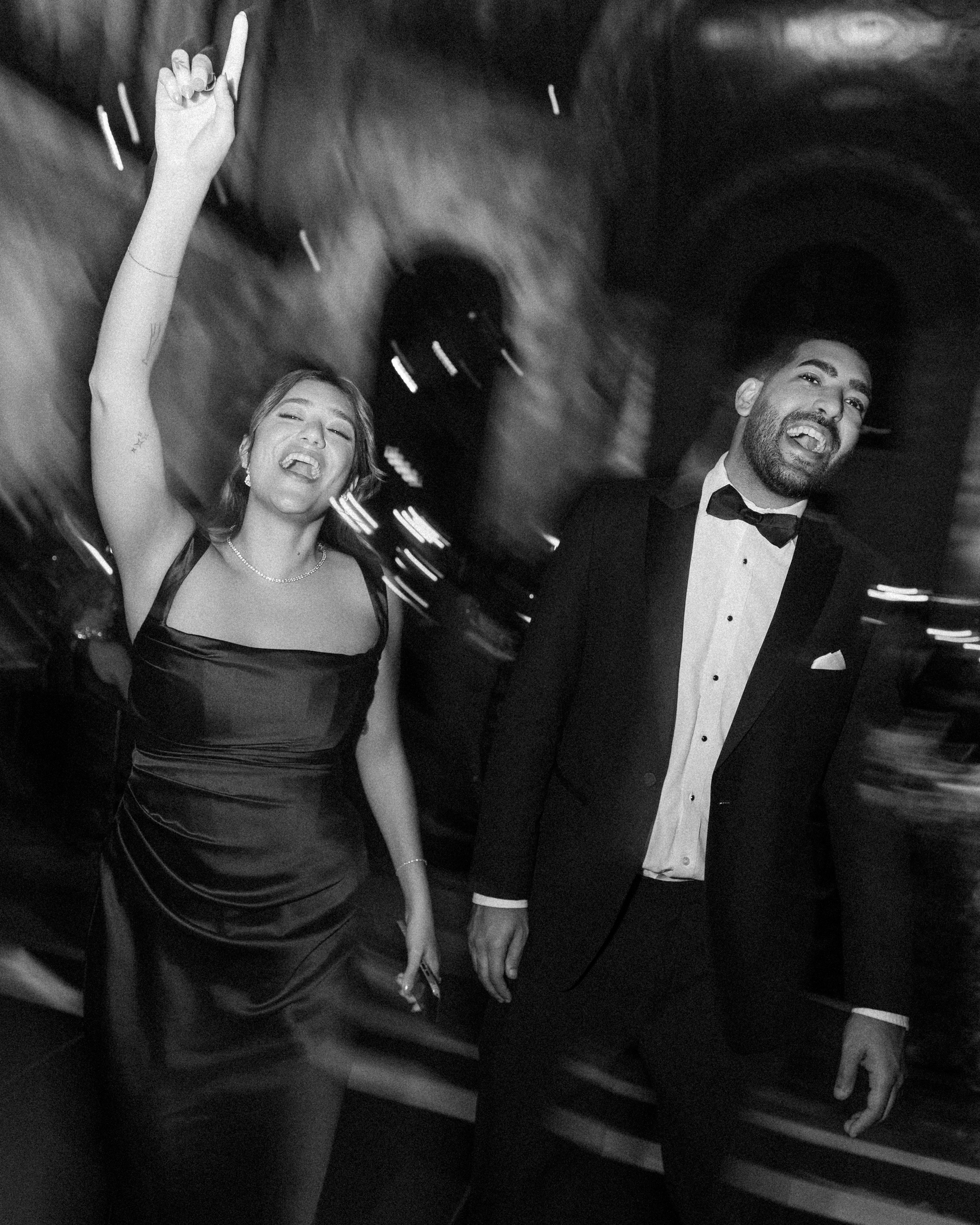 A person in an evening gown and a person in a tuxedo laughing and dancing at a Cipriani 25 Broadway wedding.