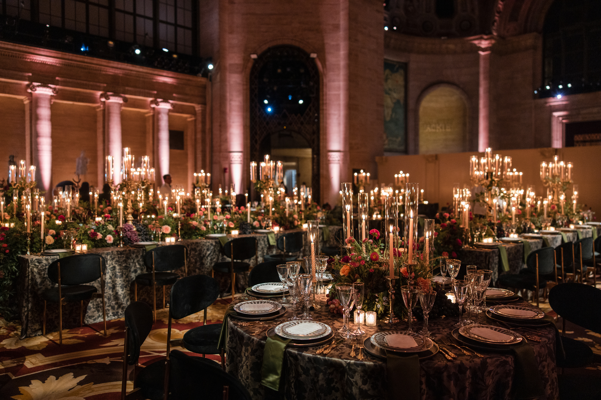 A Cipriani 25 Broadway wedding dining room with multiple round tables set for a banquet, illuminated by tall candelabras and floral centerpieces.