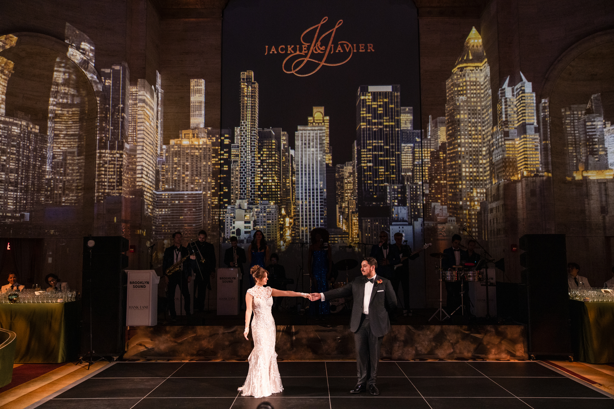 A bride and groom dance on stage at a Cipriani 25 Broadway wedding in front of a large projection of the New York City skyline. A bride and groom dance on stage at a Cipriani 25 Broadway wedding in front of a large projection of the New York City skyline.