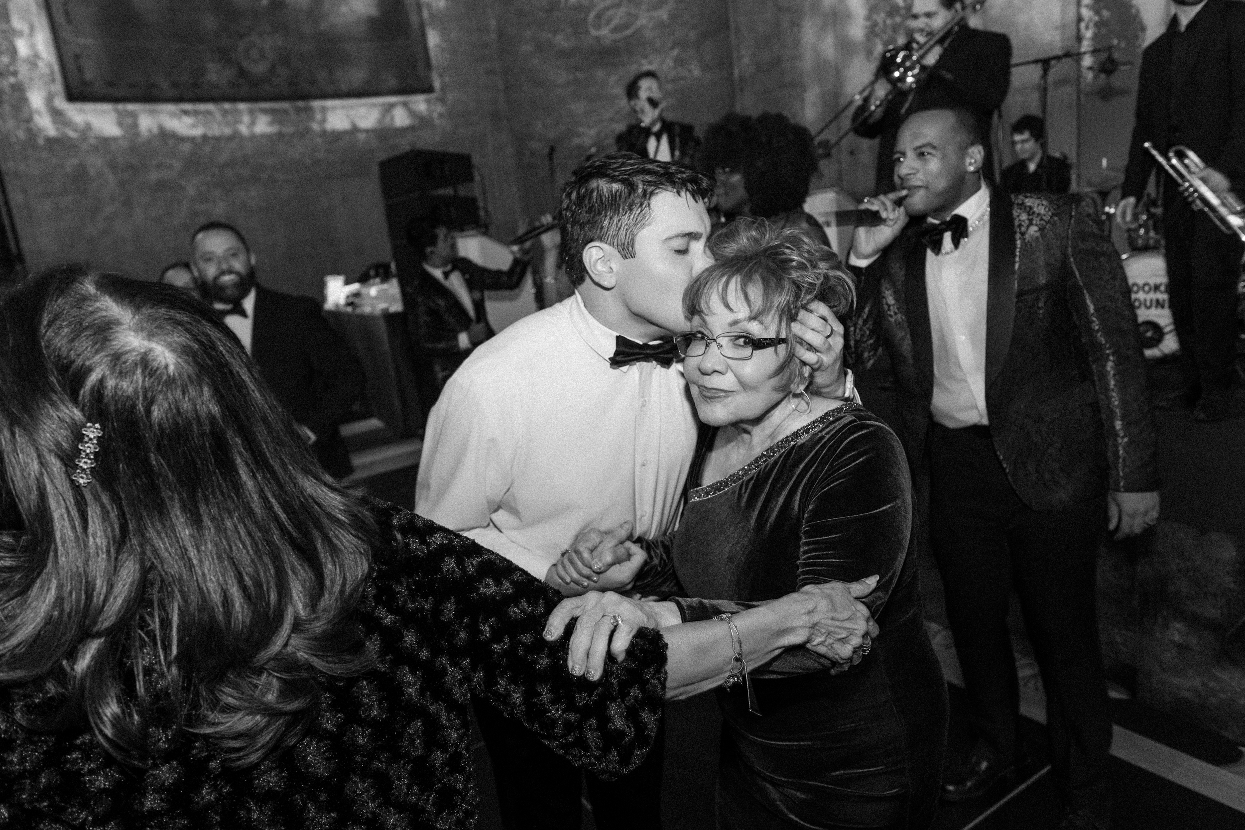 A young man kisses an older woman on the forehead as they dance at a Cipriani 25 Broadway wedding, with a band playing in the background. A young man kisses an older woman on the forehead as they dance at a Cipriani 25 Broadway wedding, with a band playing in the background.