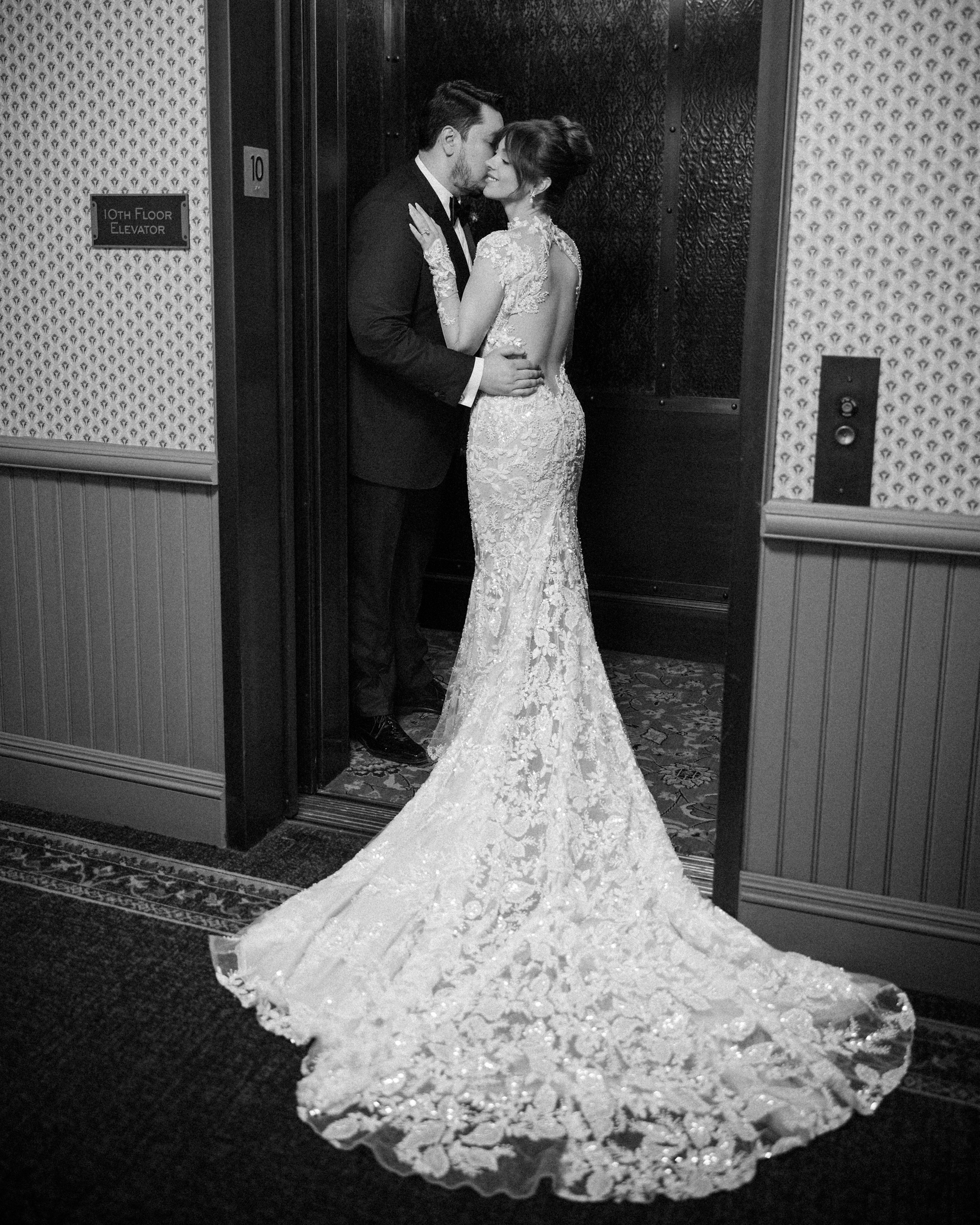 A bride in a lace wedding dress and a groom in a suit kissing inside an elevator at their Cipriani 25 Broadway wedding.